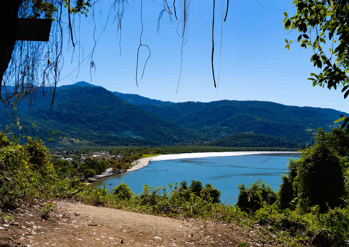 A bay and a long sandy beach below forested hills near Paraty, seen from a dirt path
