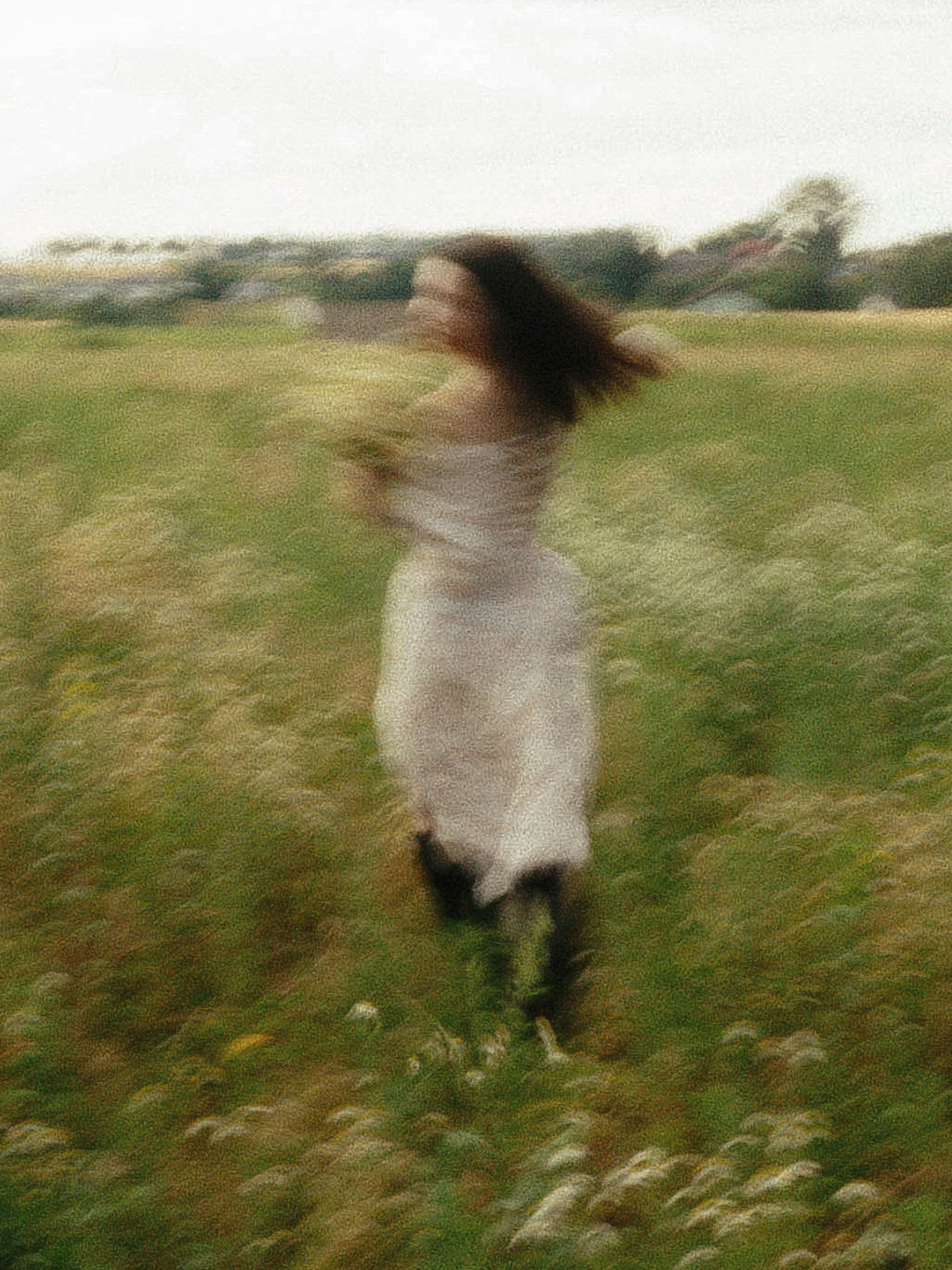 A blurred woman in a white dress running through a green meadow