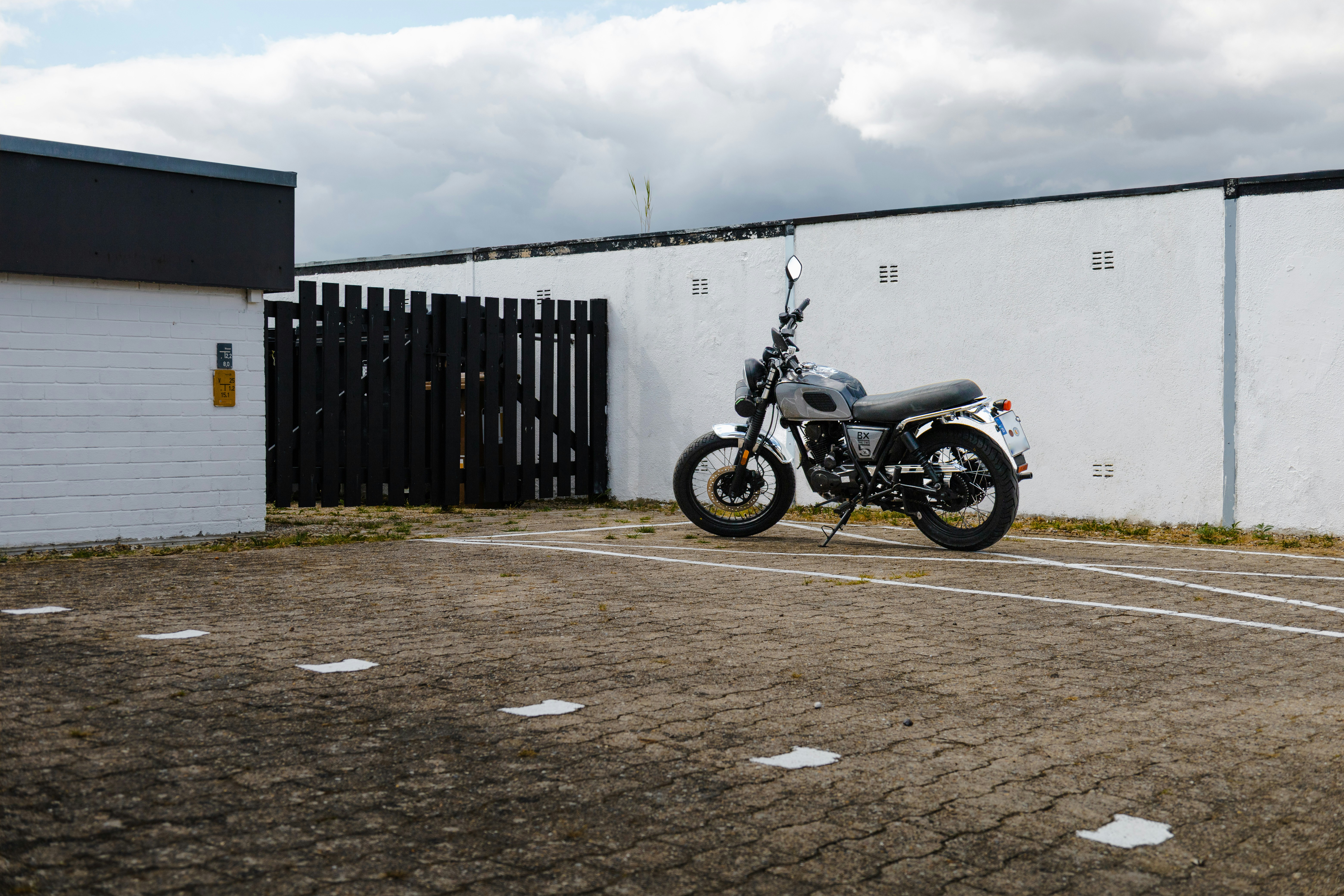 Ein graues Motorrad, das auf einem gepflasterten Grundstück an einer weißen Wand geparkt war
