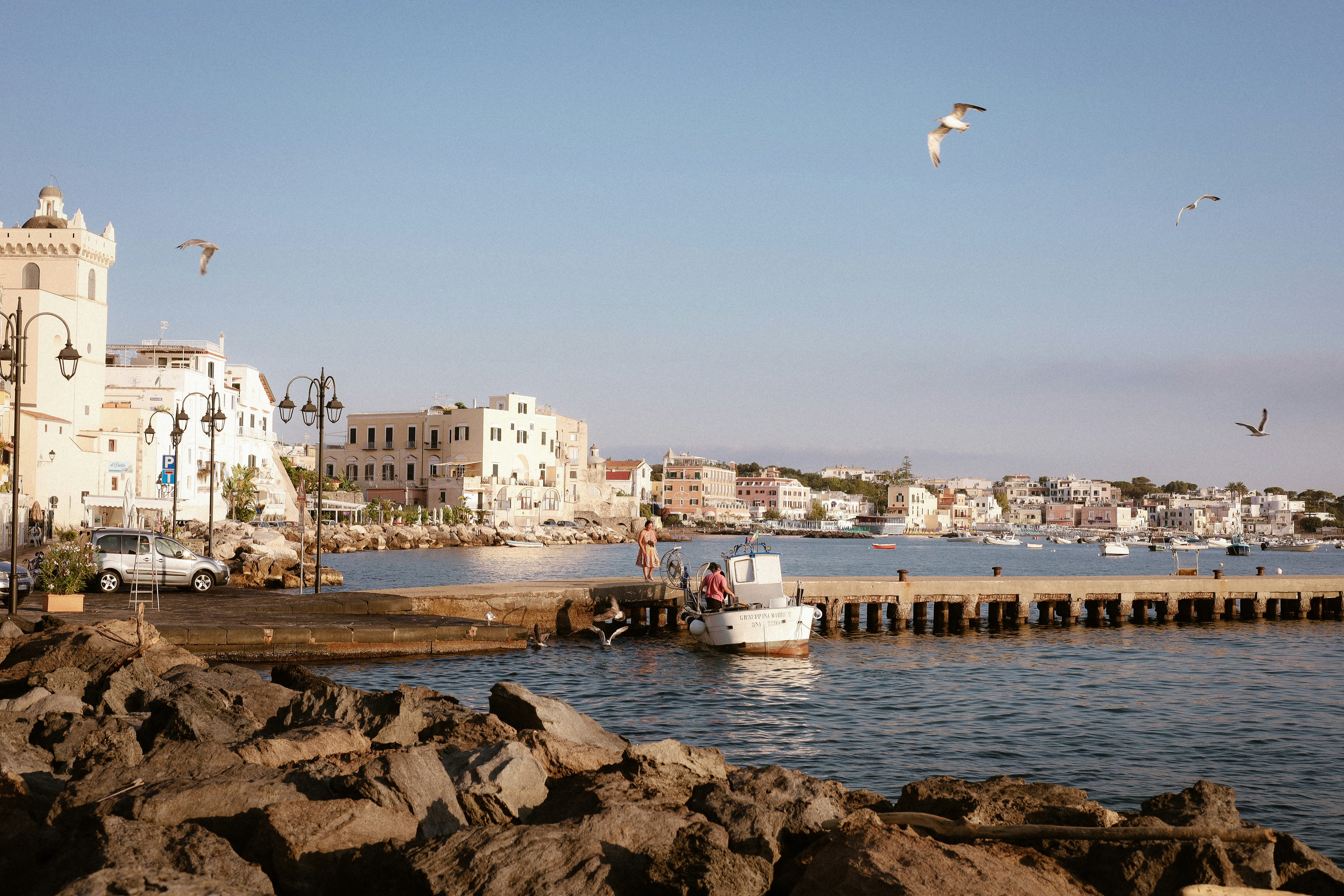 A small boat docked at a stone pier in a coastal town with seagulls