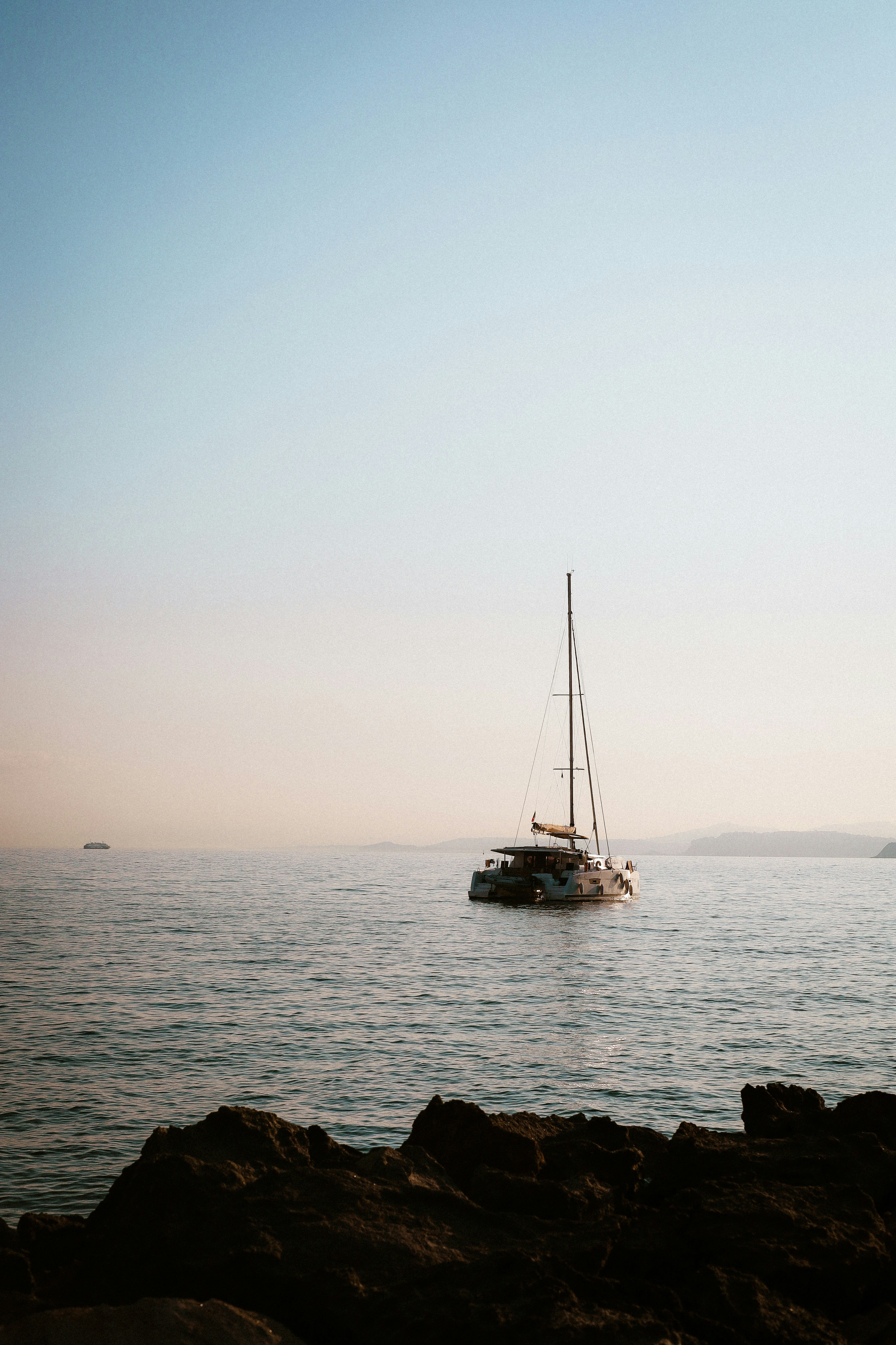 A catamaran sailing on calm water near a rocky shoreline