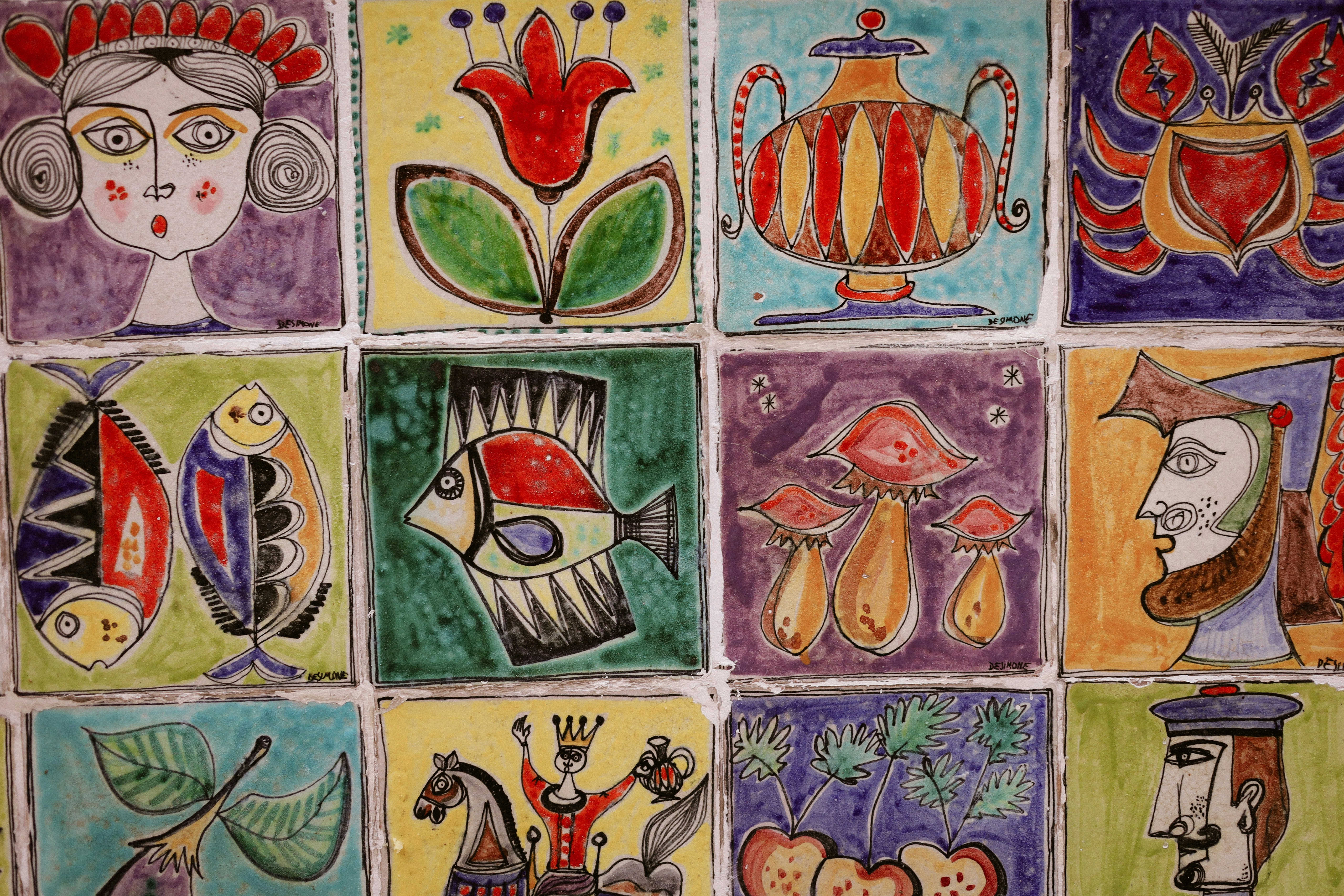 A grid of colorful ceramic tiles featuring hand-painted illustrations of people, fish, and plants
