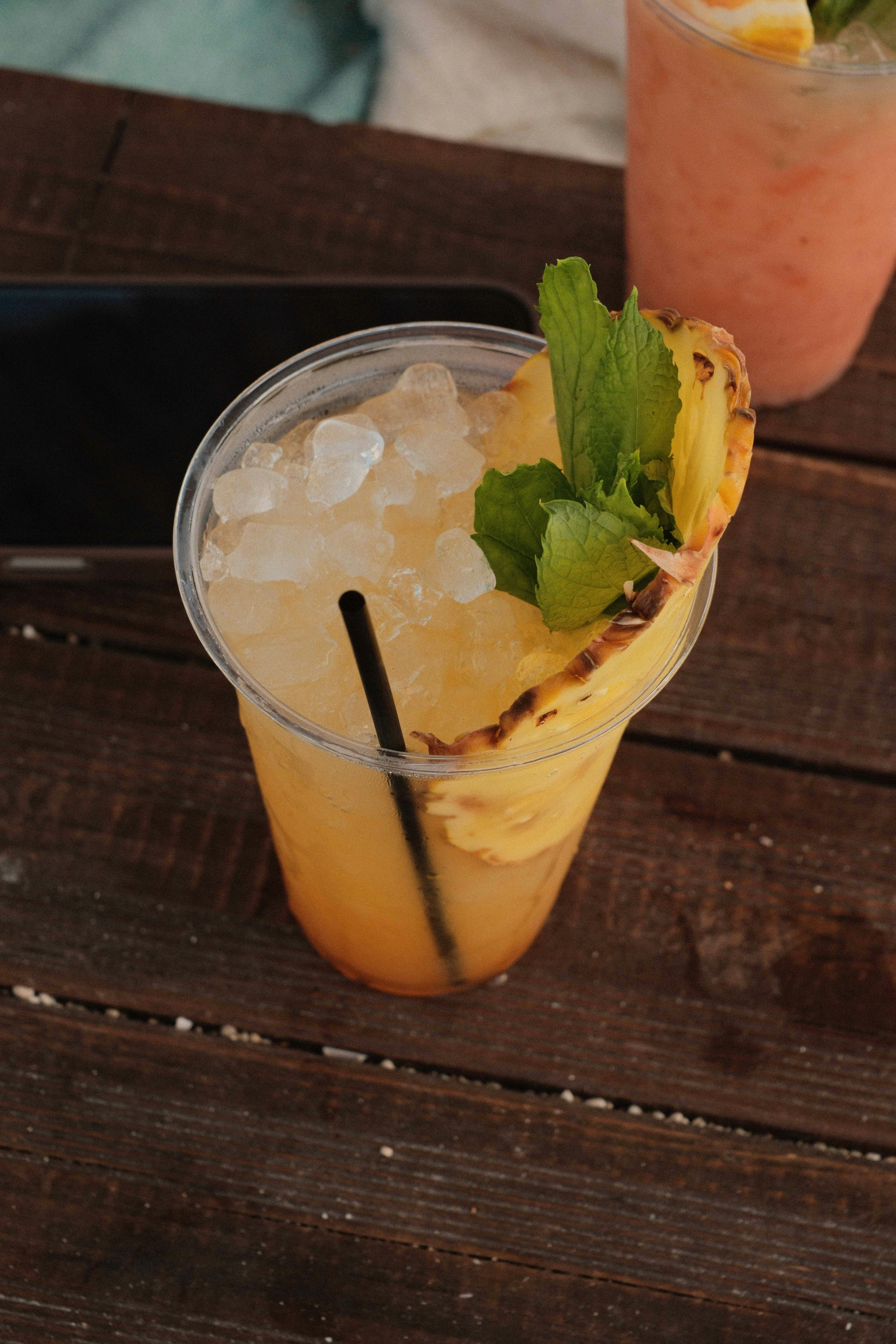 A pineapple cocktail with crushed ice, a straw, and mint on a wooden table.