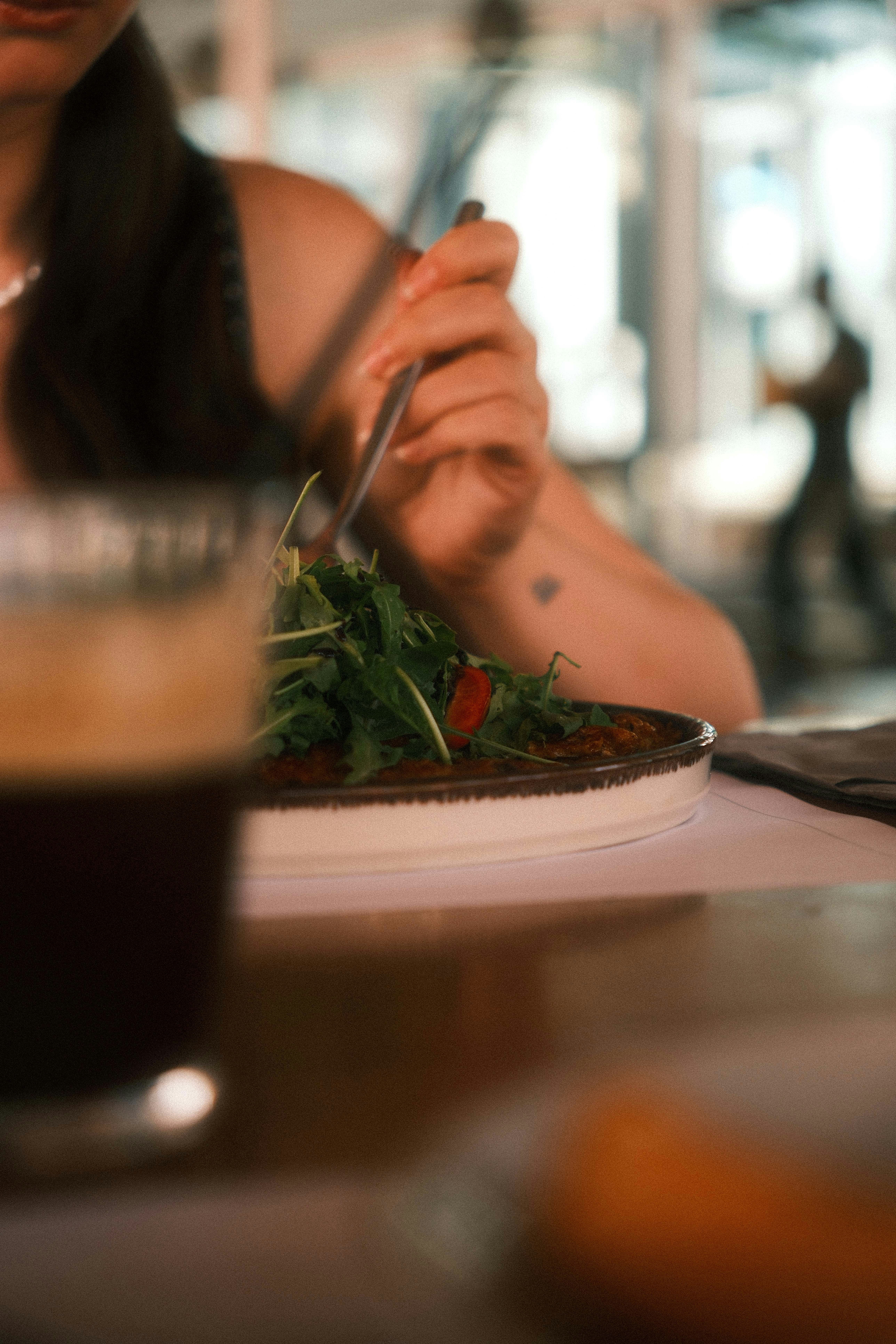 A person eating a salad with arugula and tomatoes at a restaurant table