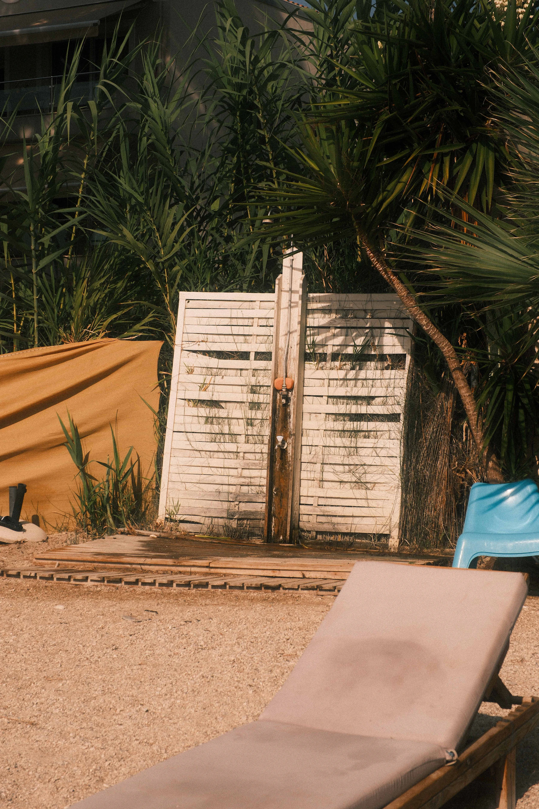 Outdoor shower with a white timber privacy screen on a sandy beach