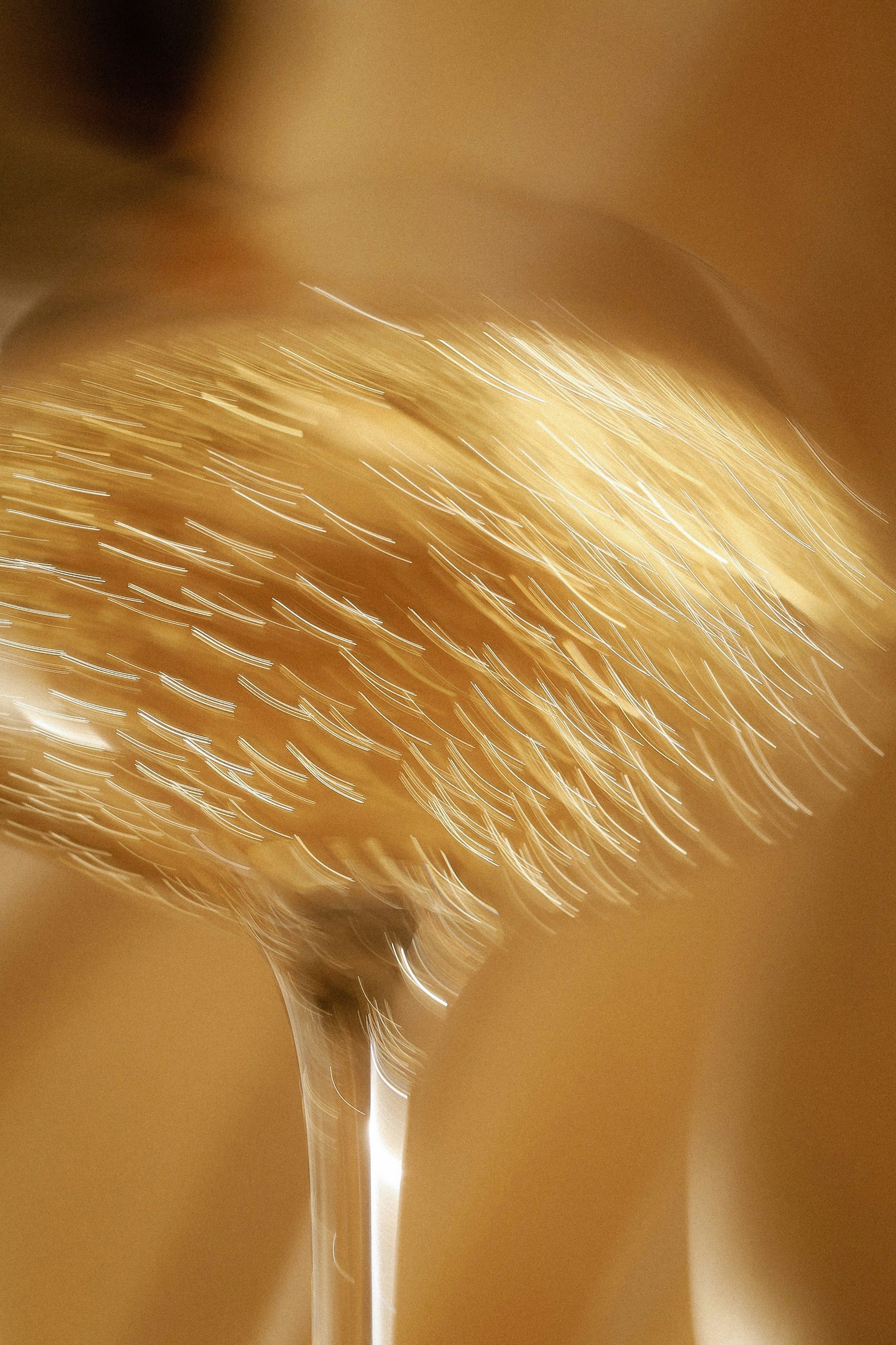 A makeup brush with golden bristles captured in motion against a warm background.