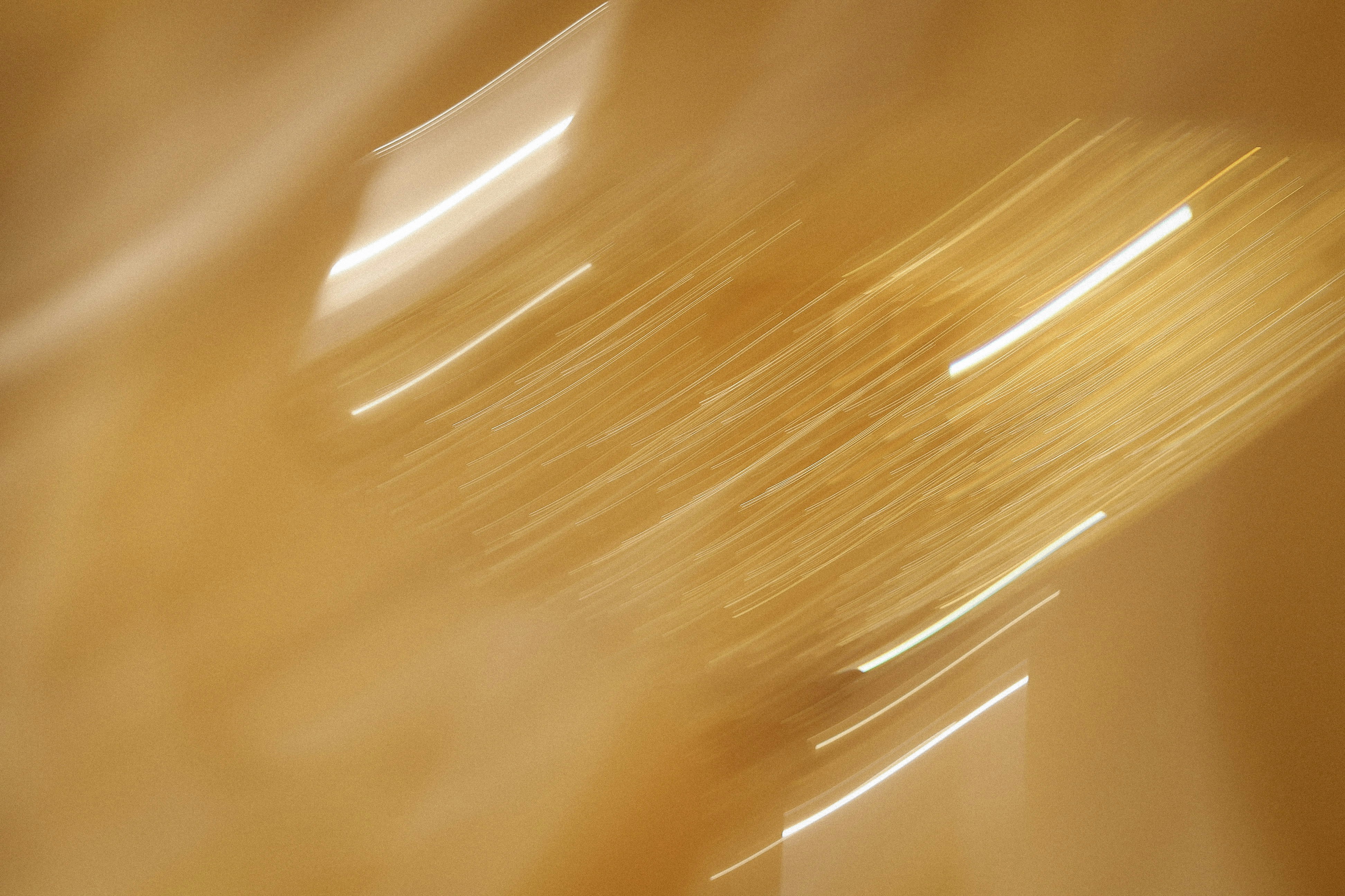 Abstract motion blur of golden light streaks against a warm tan background