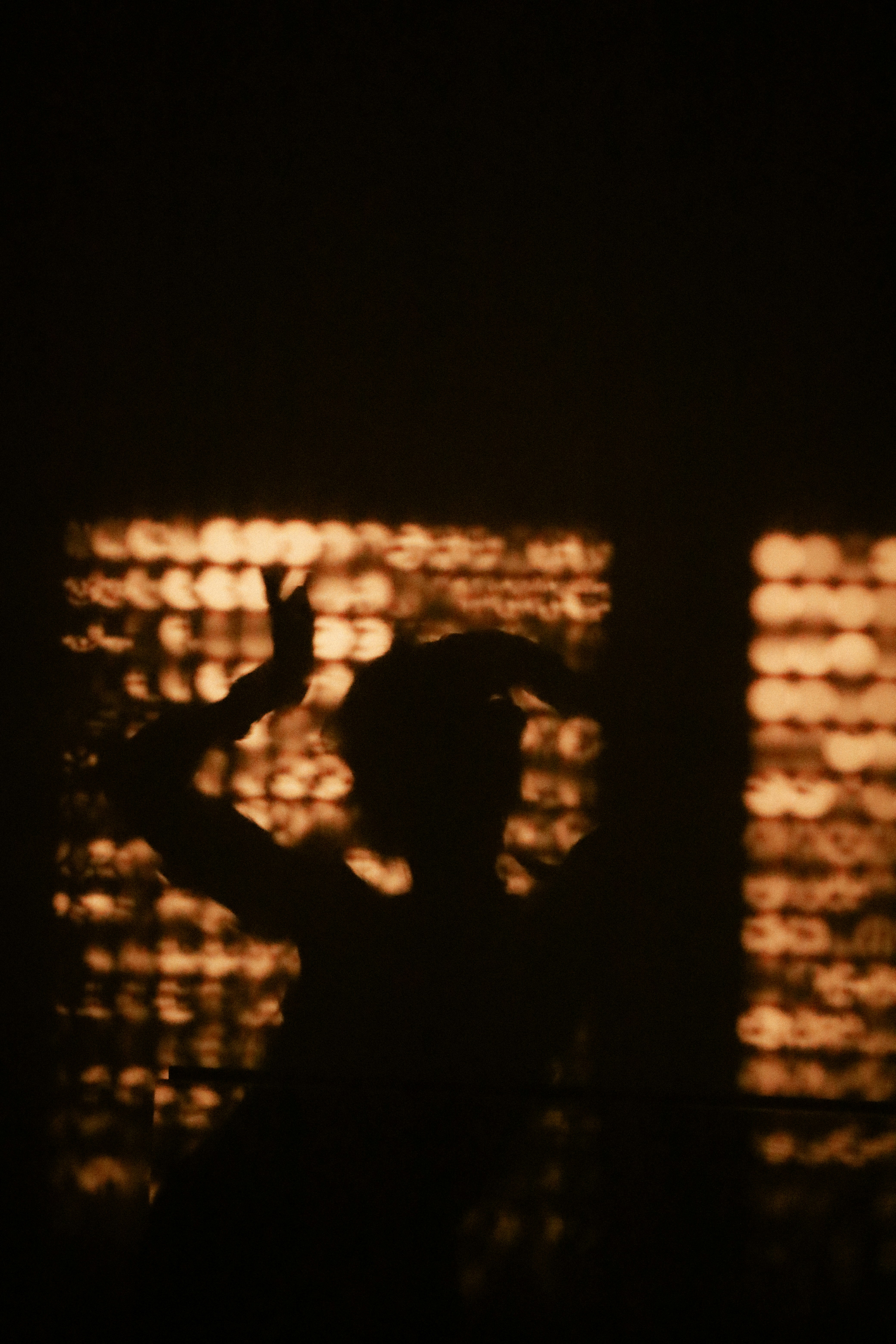 A person in silhouette dancing against a background of warm glowing bokeh lights