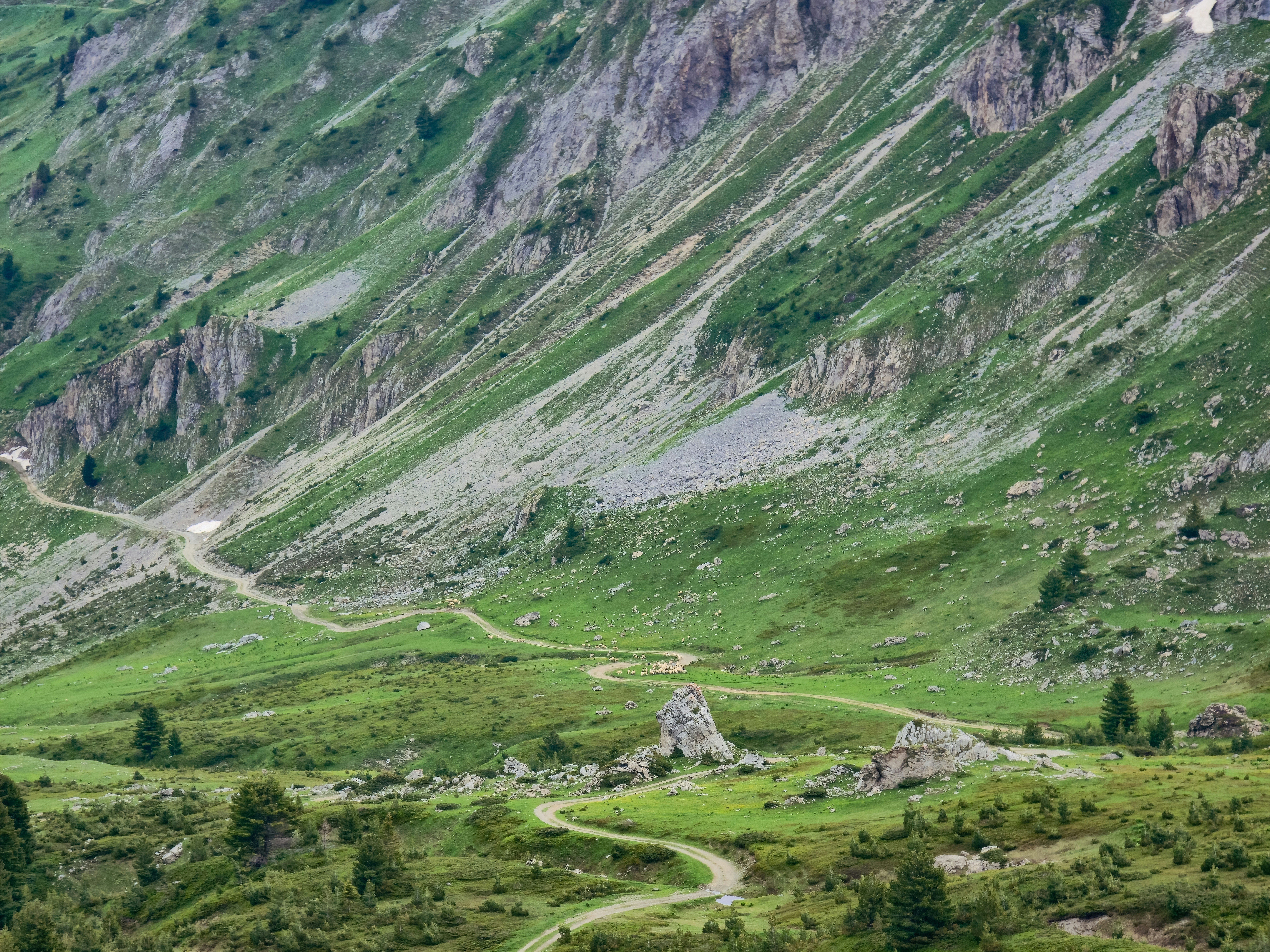 Un sendero de tierra serpenteante a través de un valle montañoso verde con laderas rocosas.