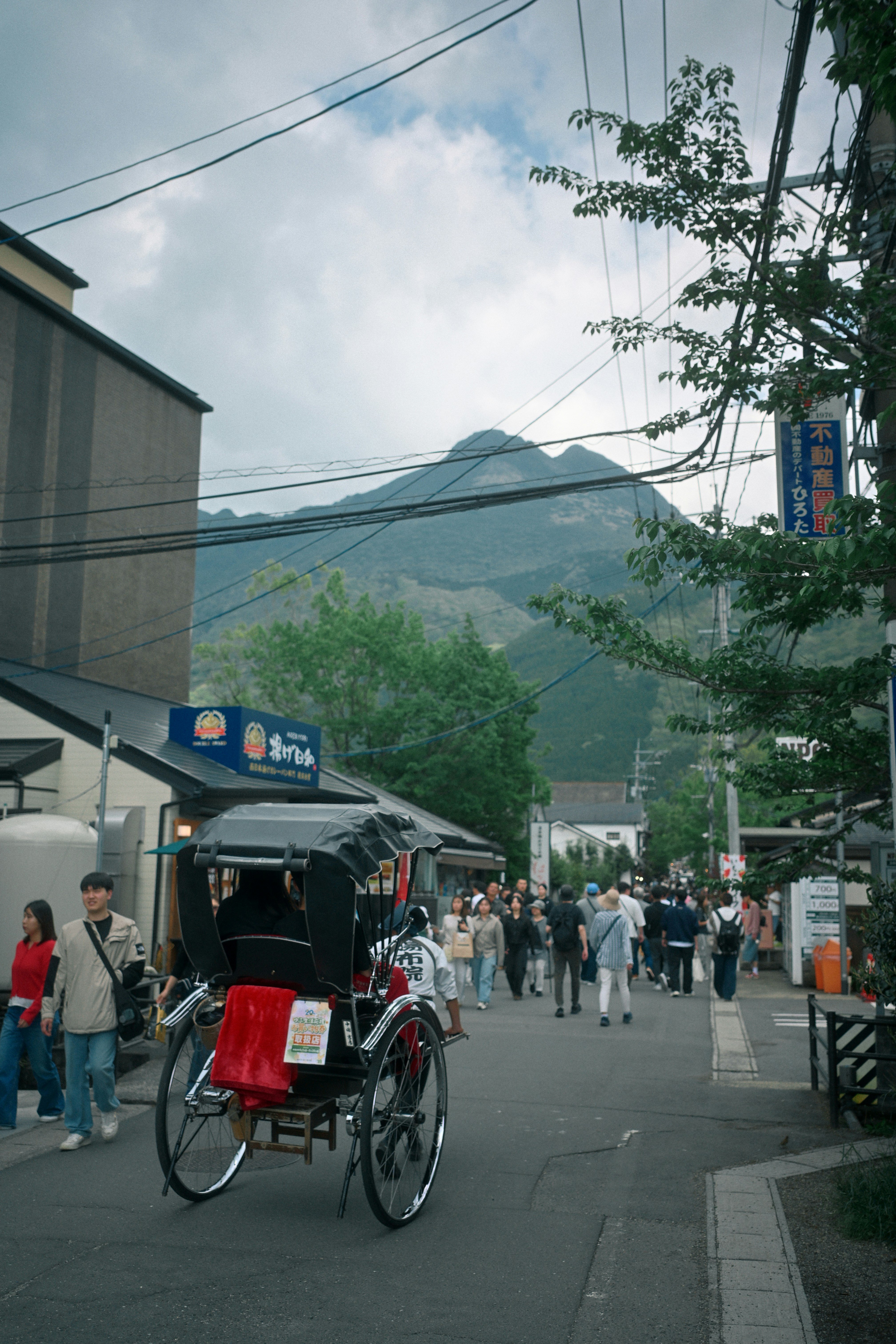 A rickshaw moving through a crowded street in Yufuin with a mountain backdrop.