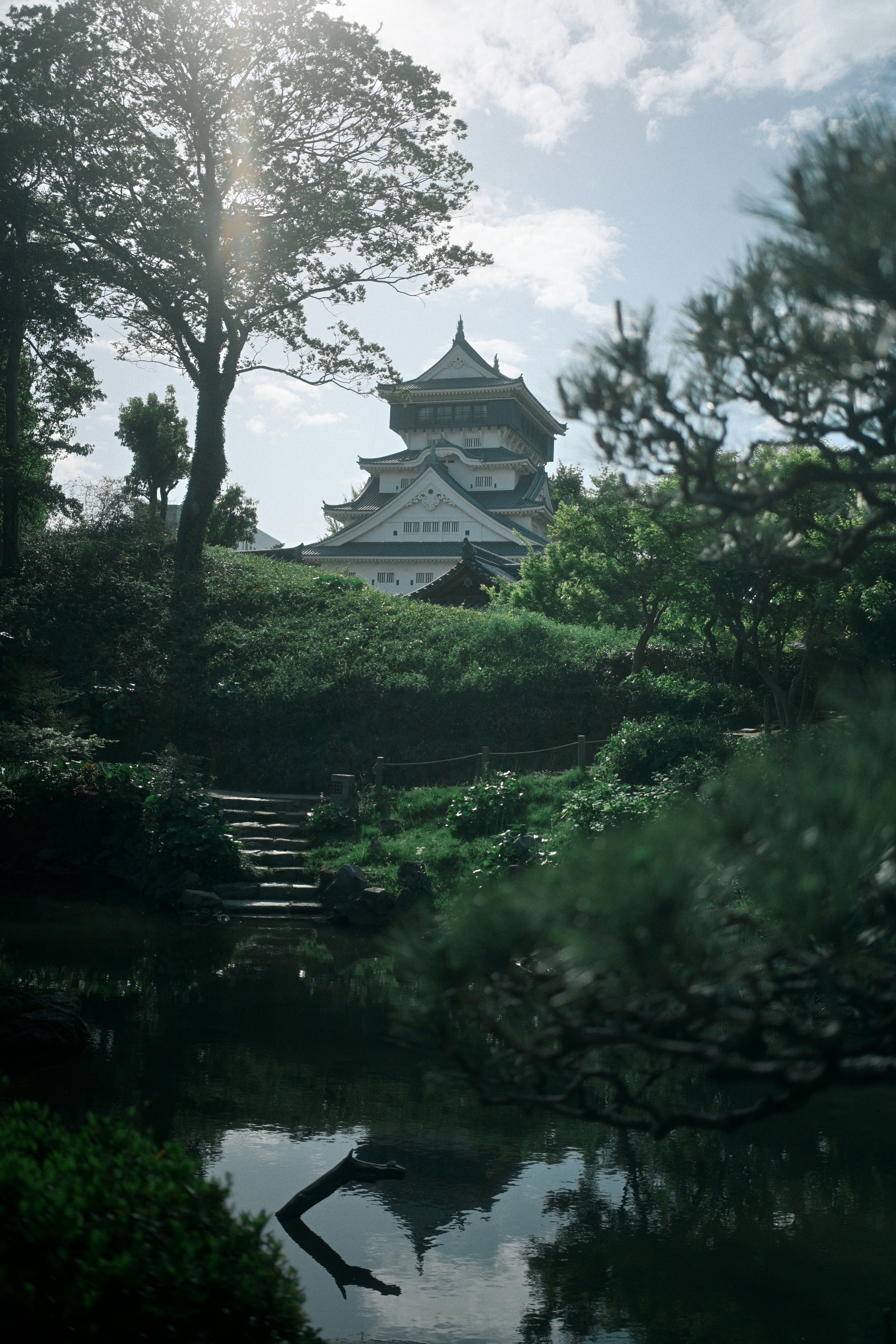 A traditional Japanese castle rising above a lush garden with a reflective pond.