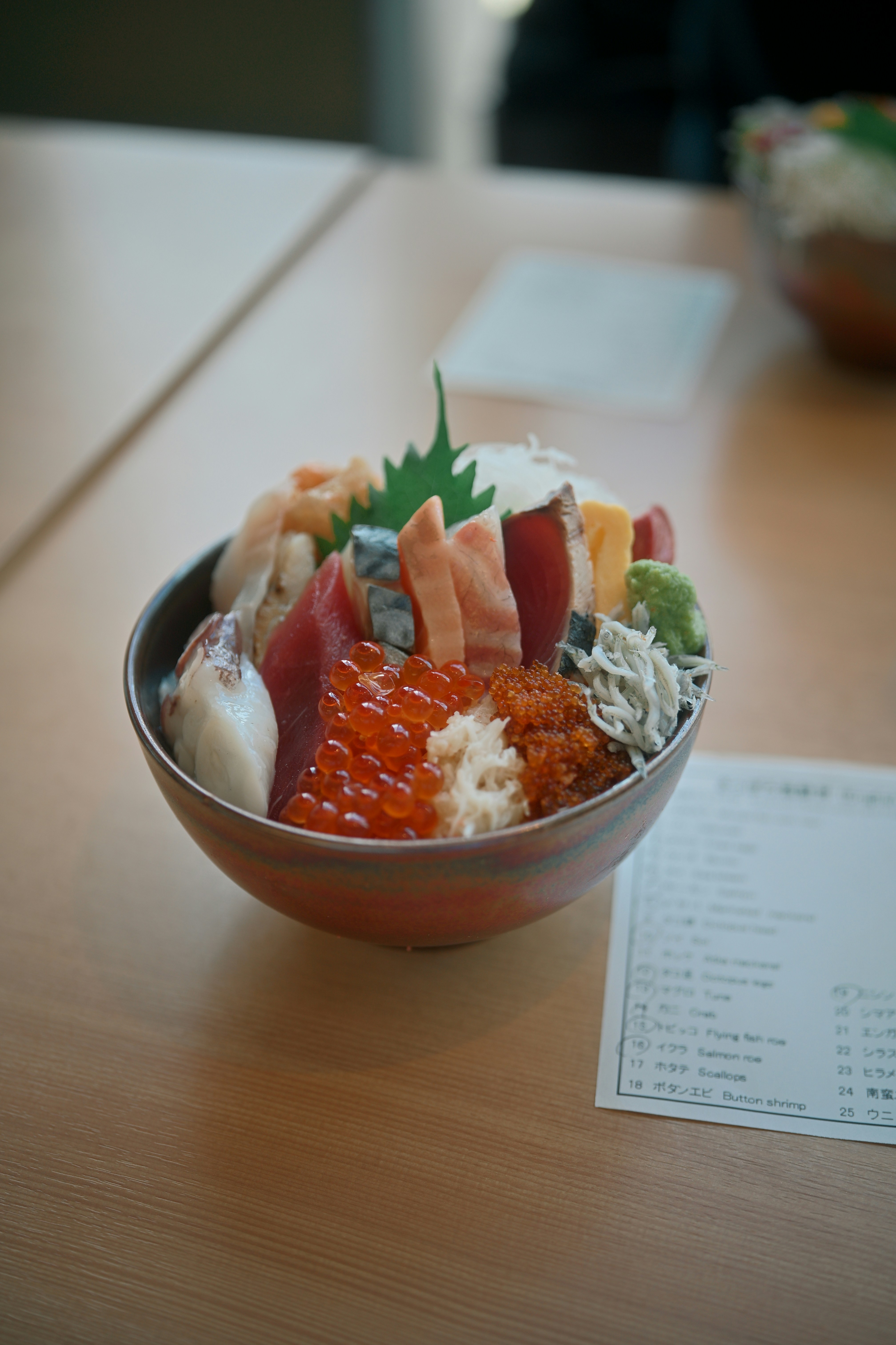 A bowl of assorted sashimi, salmon roe, and whitebait on a wooden table.