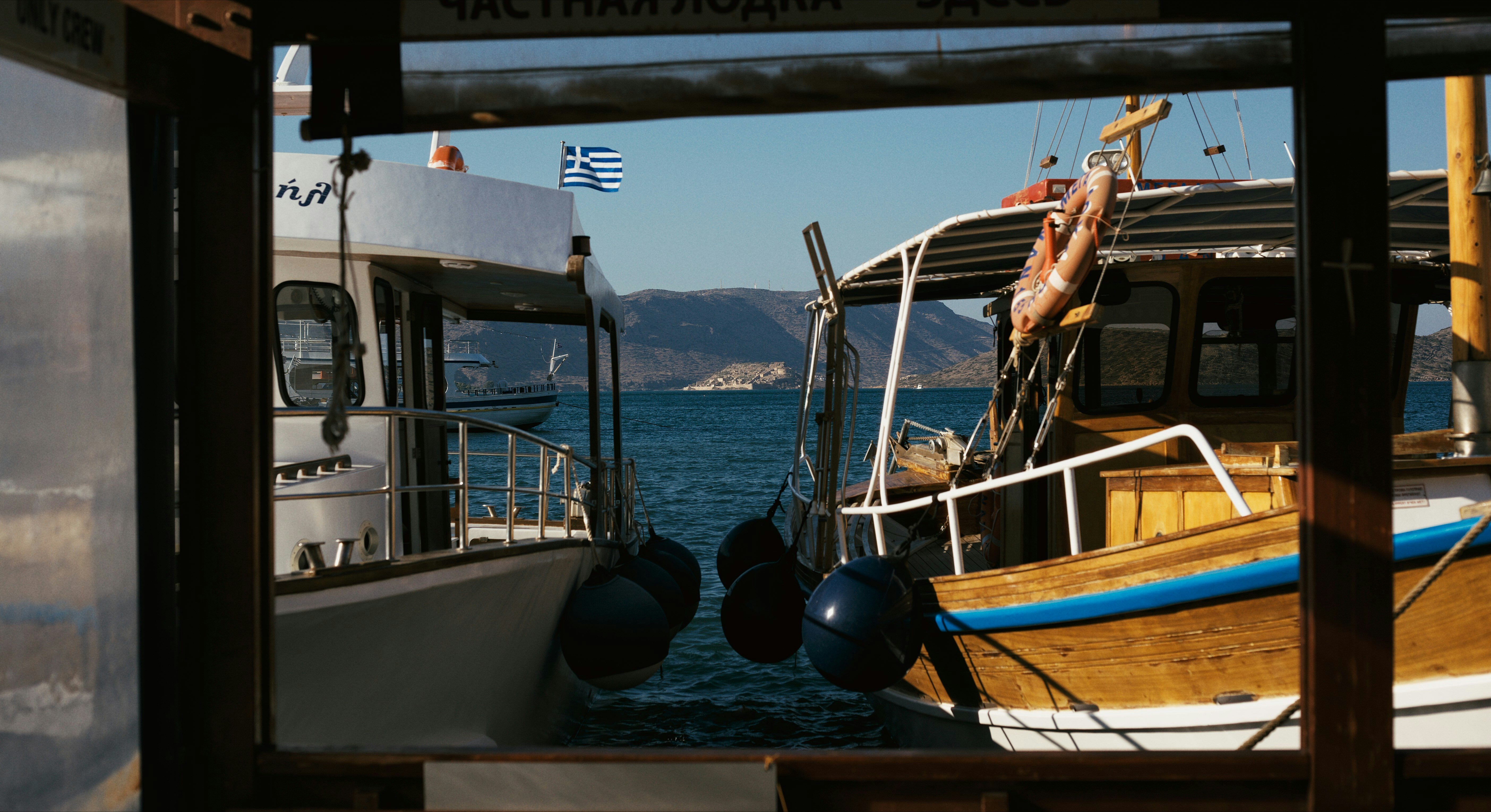 Two boats moored in a Greek harbour with a Greek flag flying behind them