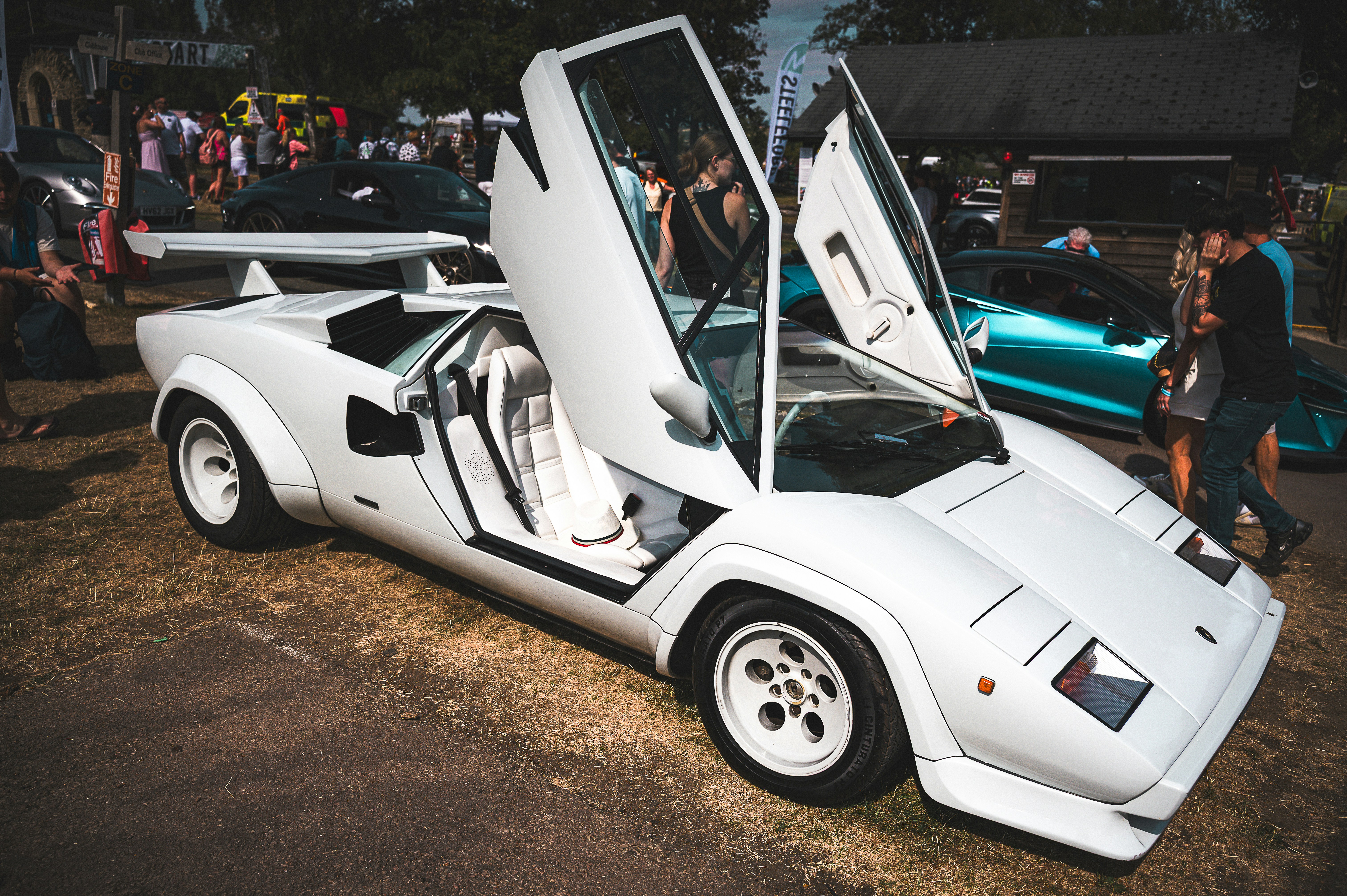 A white sports car with scissor doors open at an outdoor car show