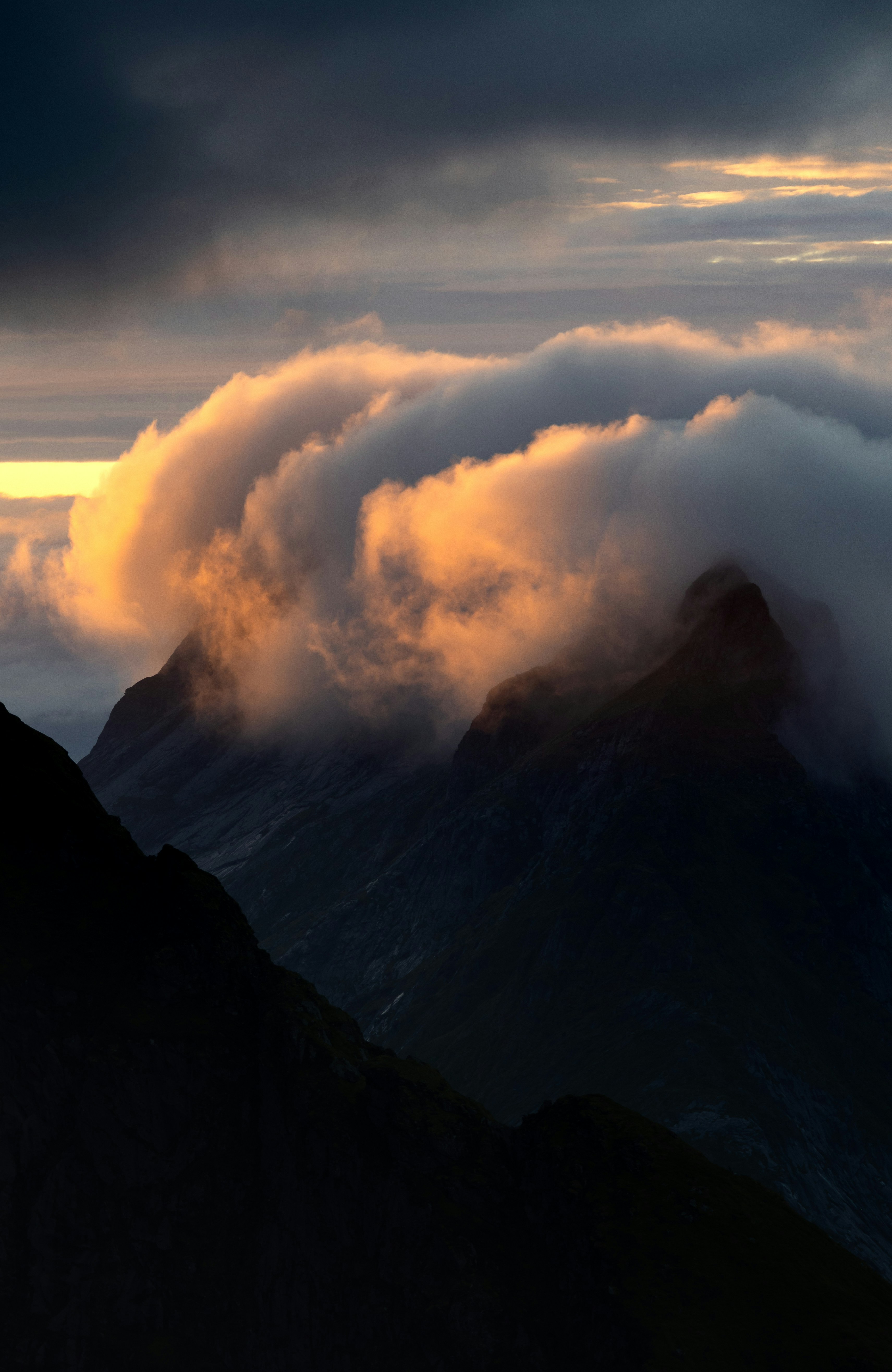 Clouds glowing with golden light clinging to dark mountain peaks at low sun.