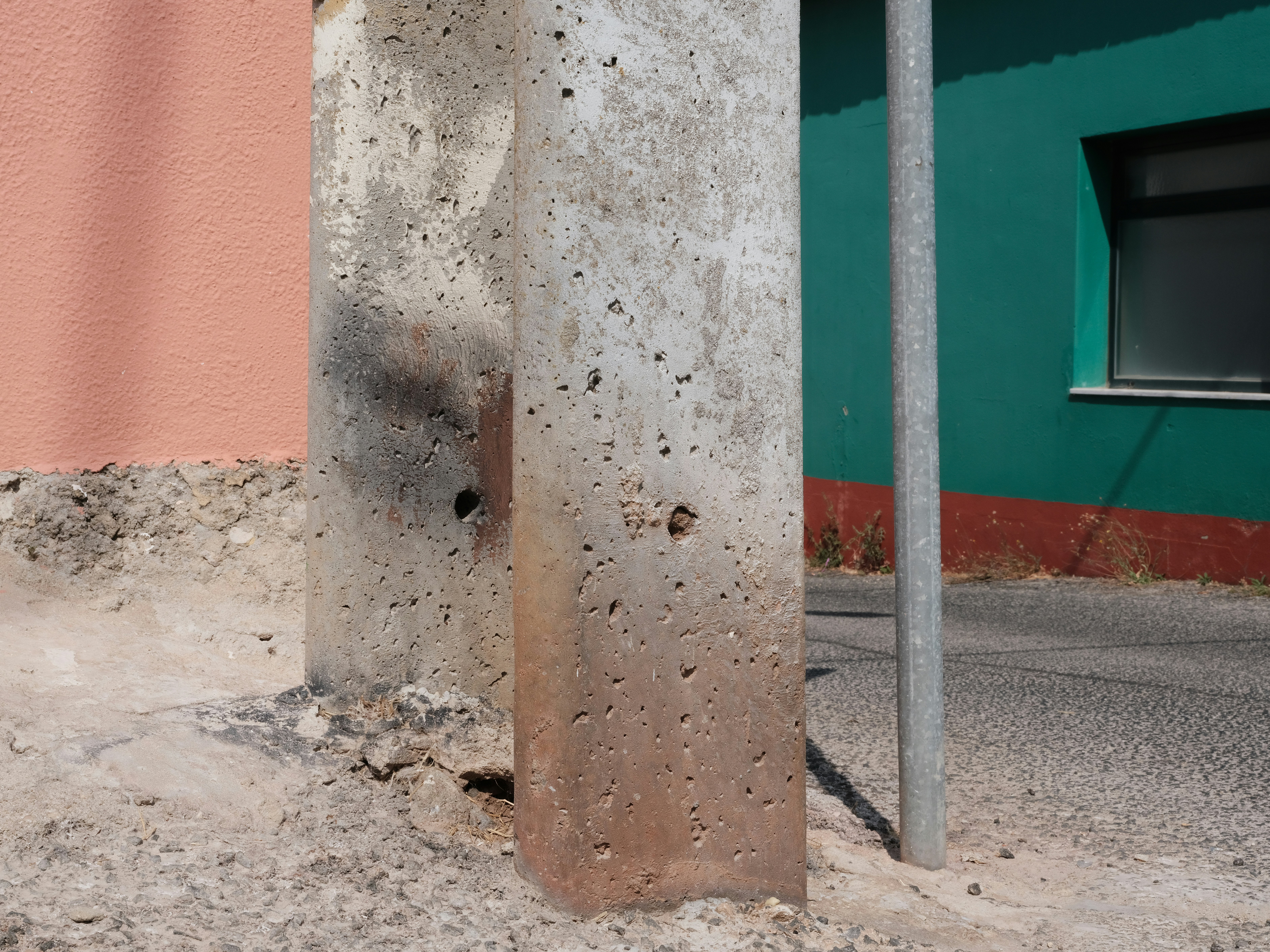 A weathered concrete pillar beside a green wall and a pink wall