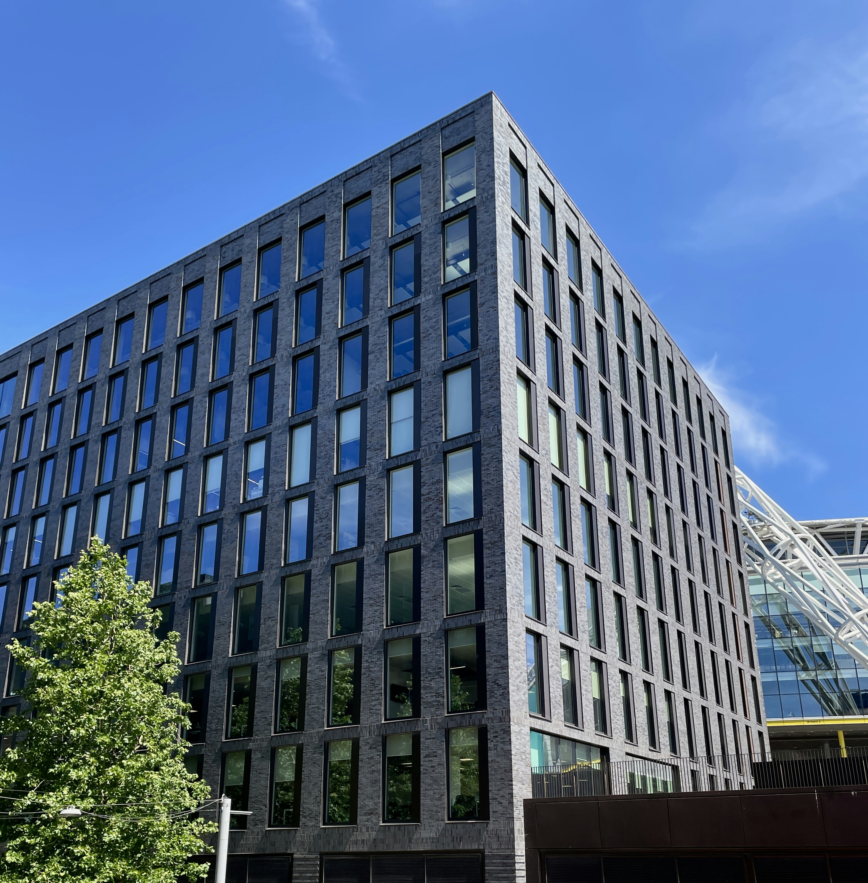 A modern dark brick office building with many rectangular windows under a blue sky