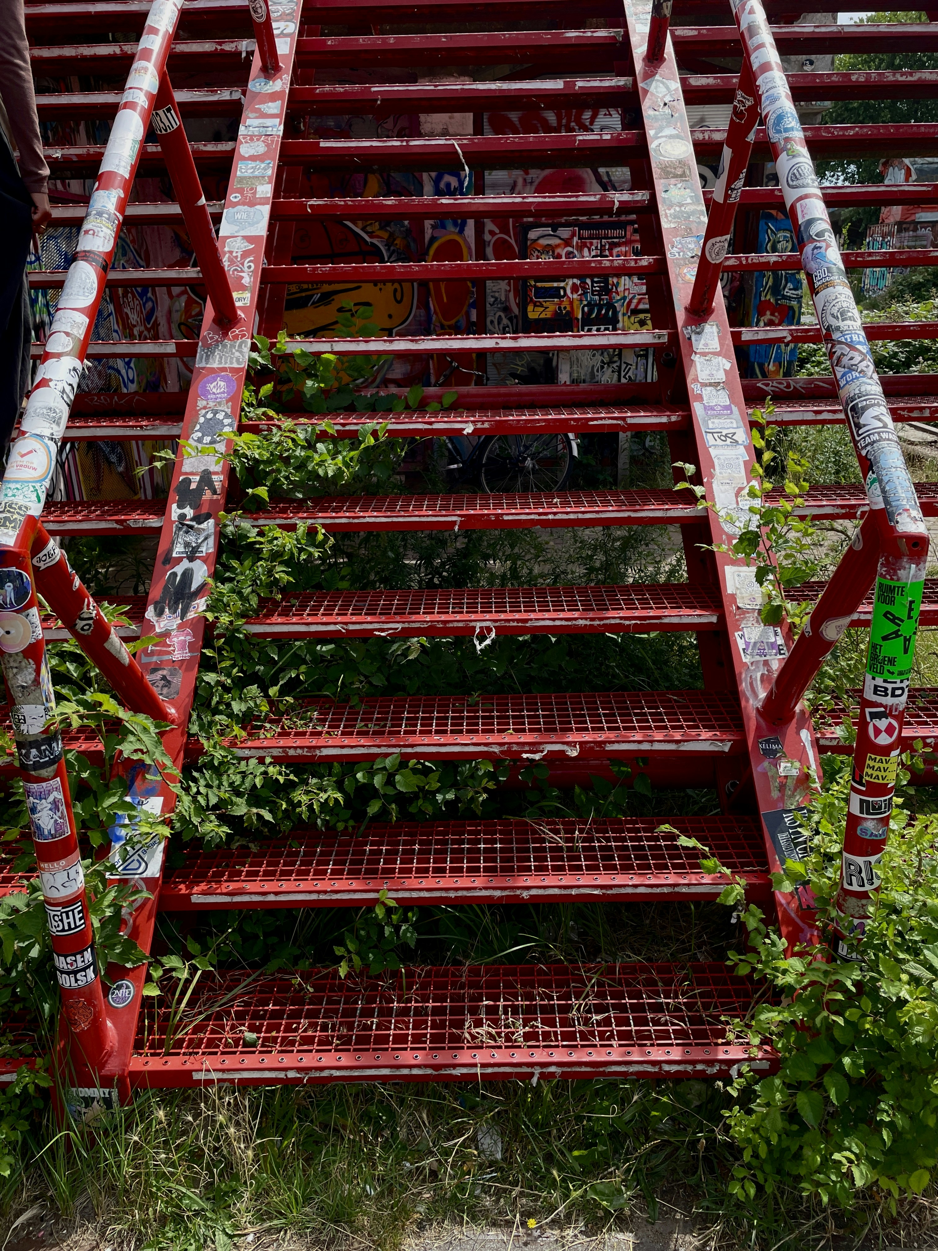 Red metal stairs covered in stickers and overgrown with green plants