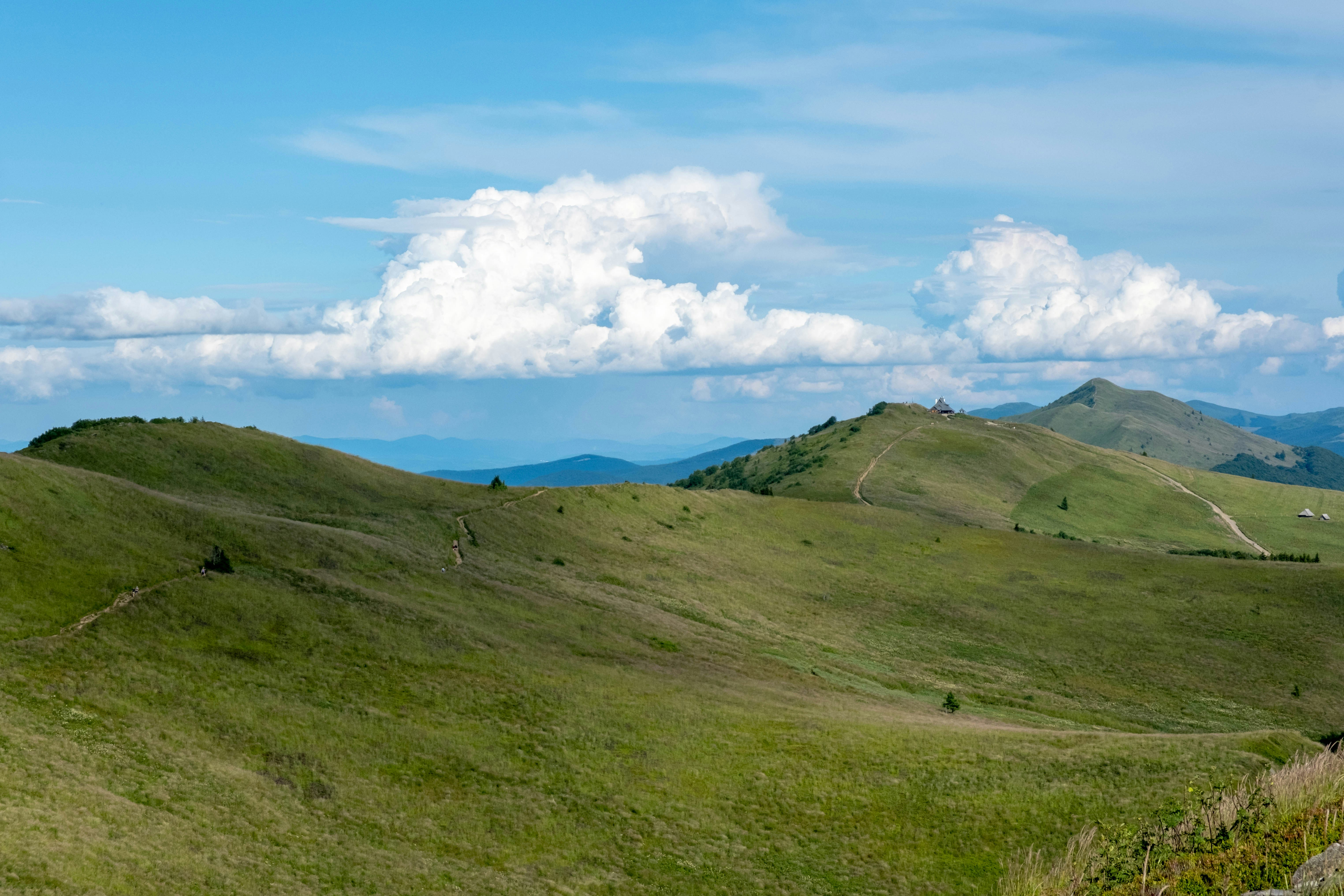 A winding dirt path across green mountain slopes under a bright blue sky