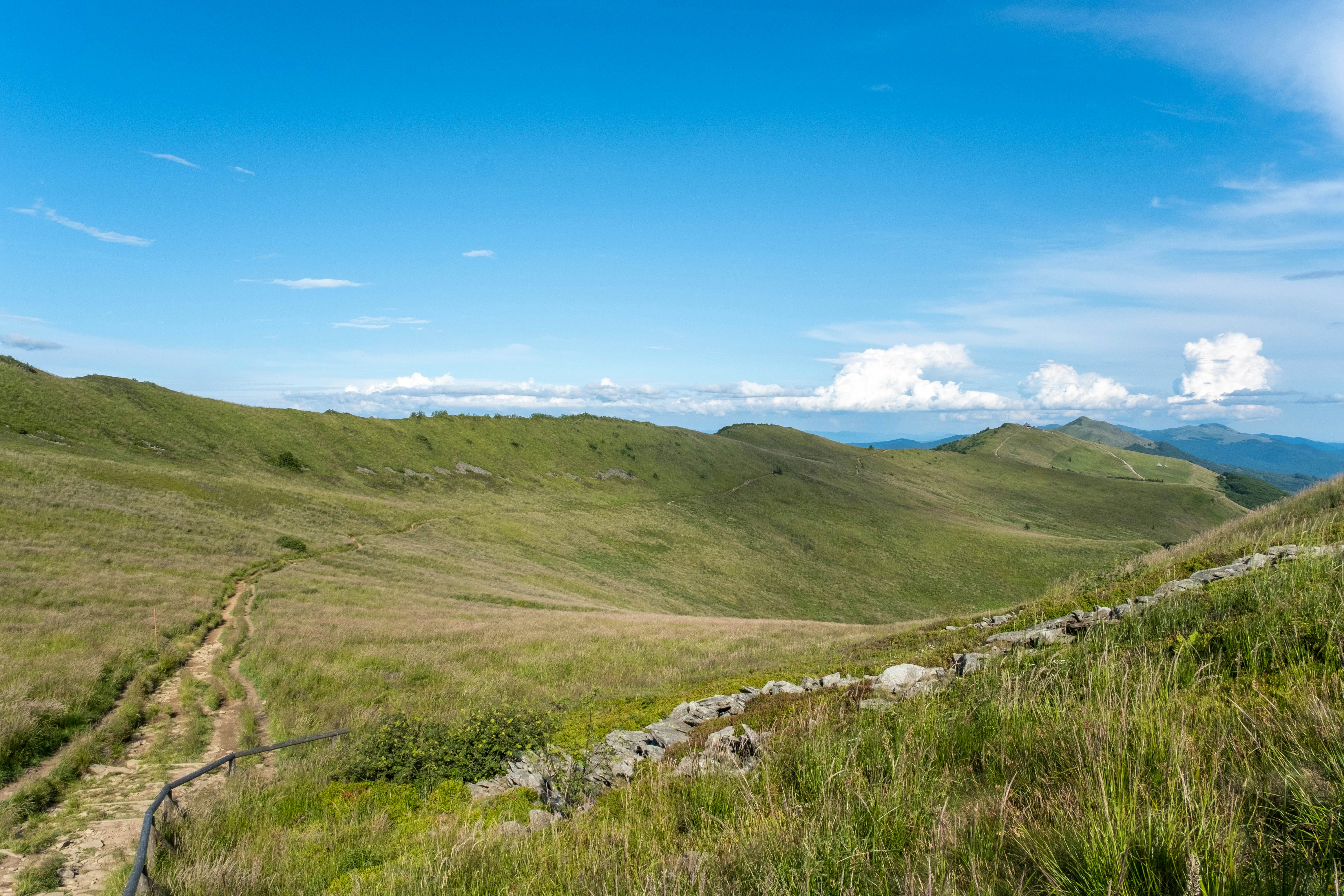 A dirt path winding through grassy mountain slopes under a bright blue sky