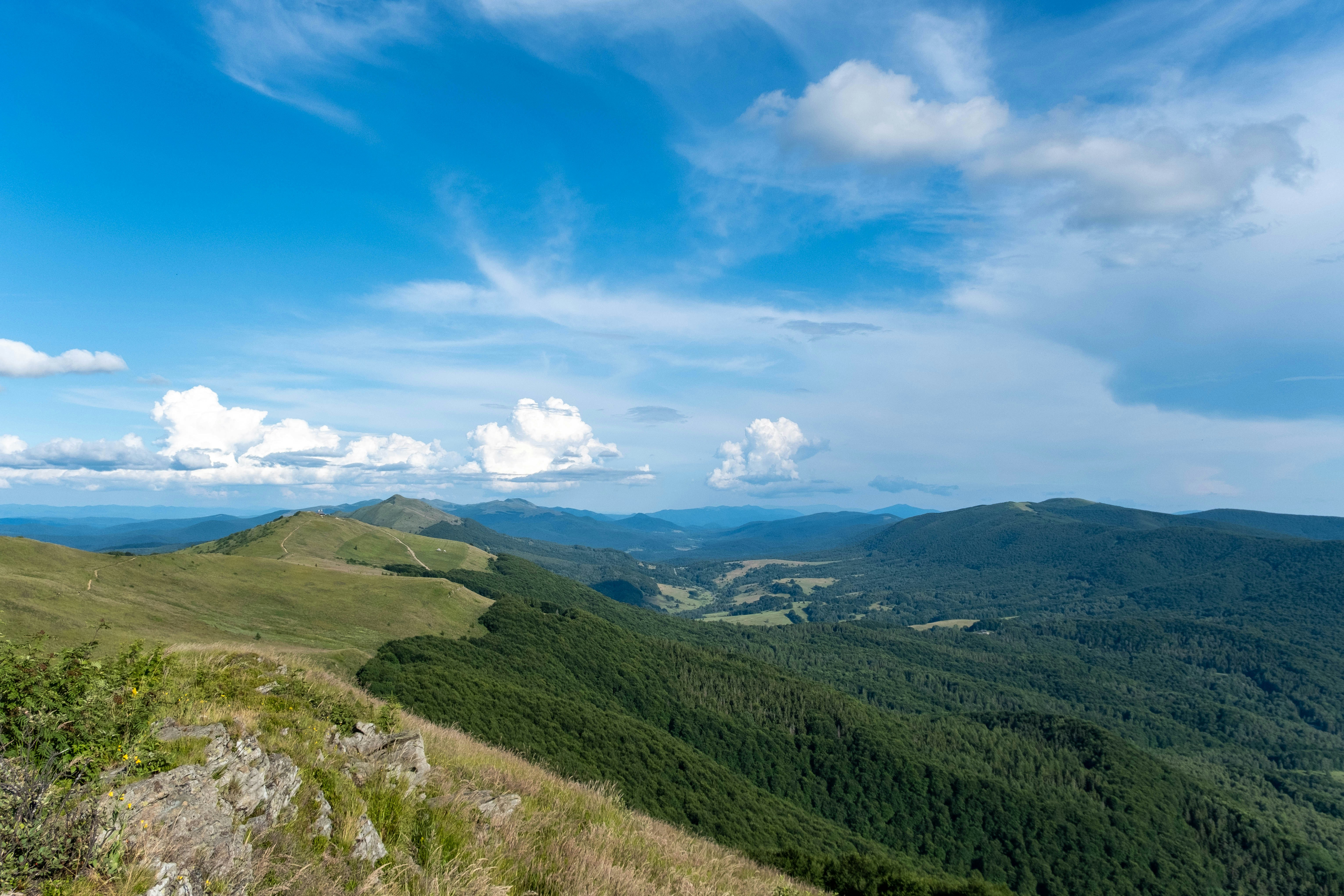 Rolling green mountain ridges under a bright blue sky with scattered white clouds
