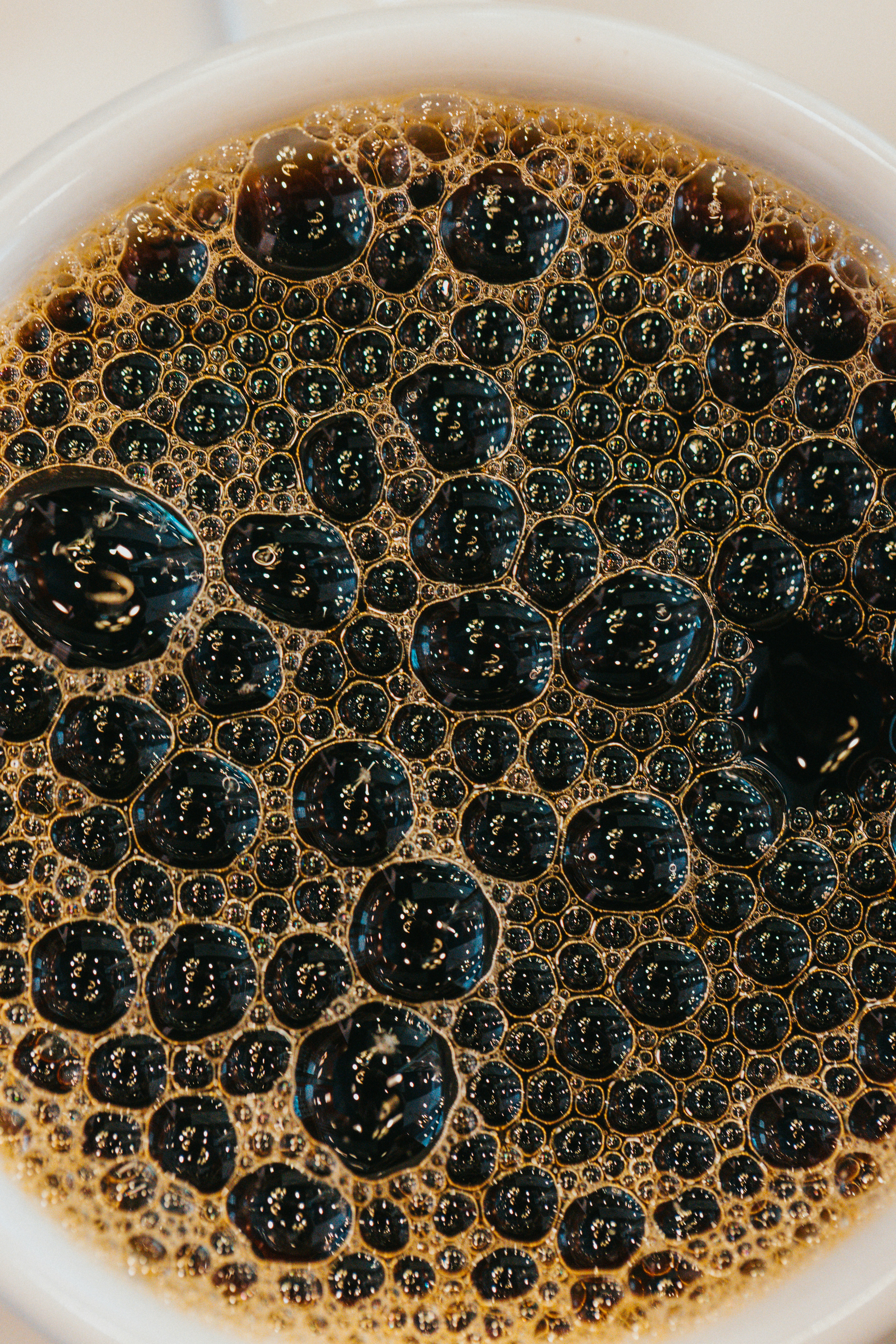 A close-up of dark coffee bubbles in a white ceramic mug.
