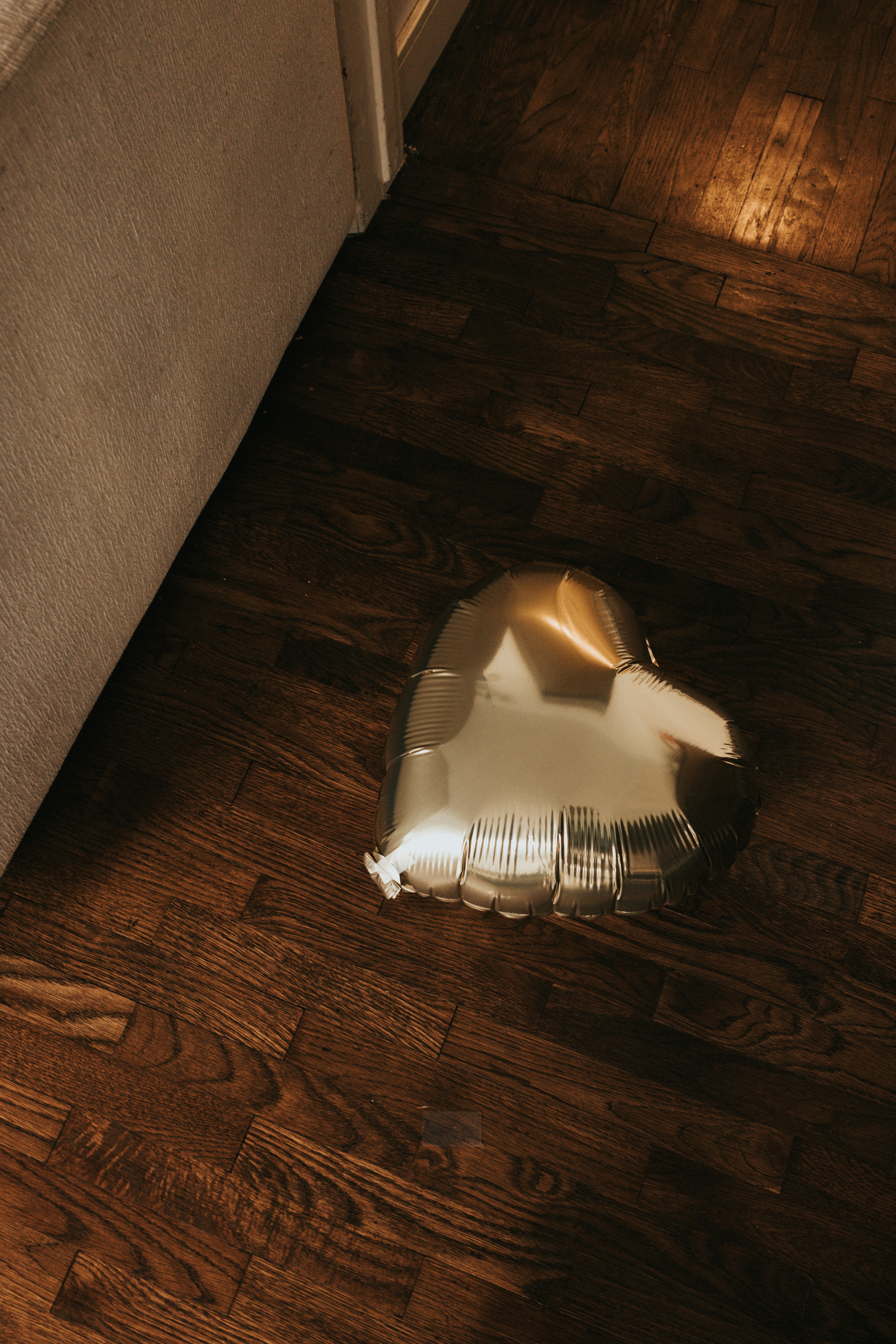 A metallic gold heart-shaped balloon on a dark wooden floor.