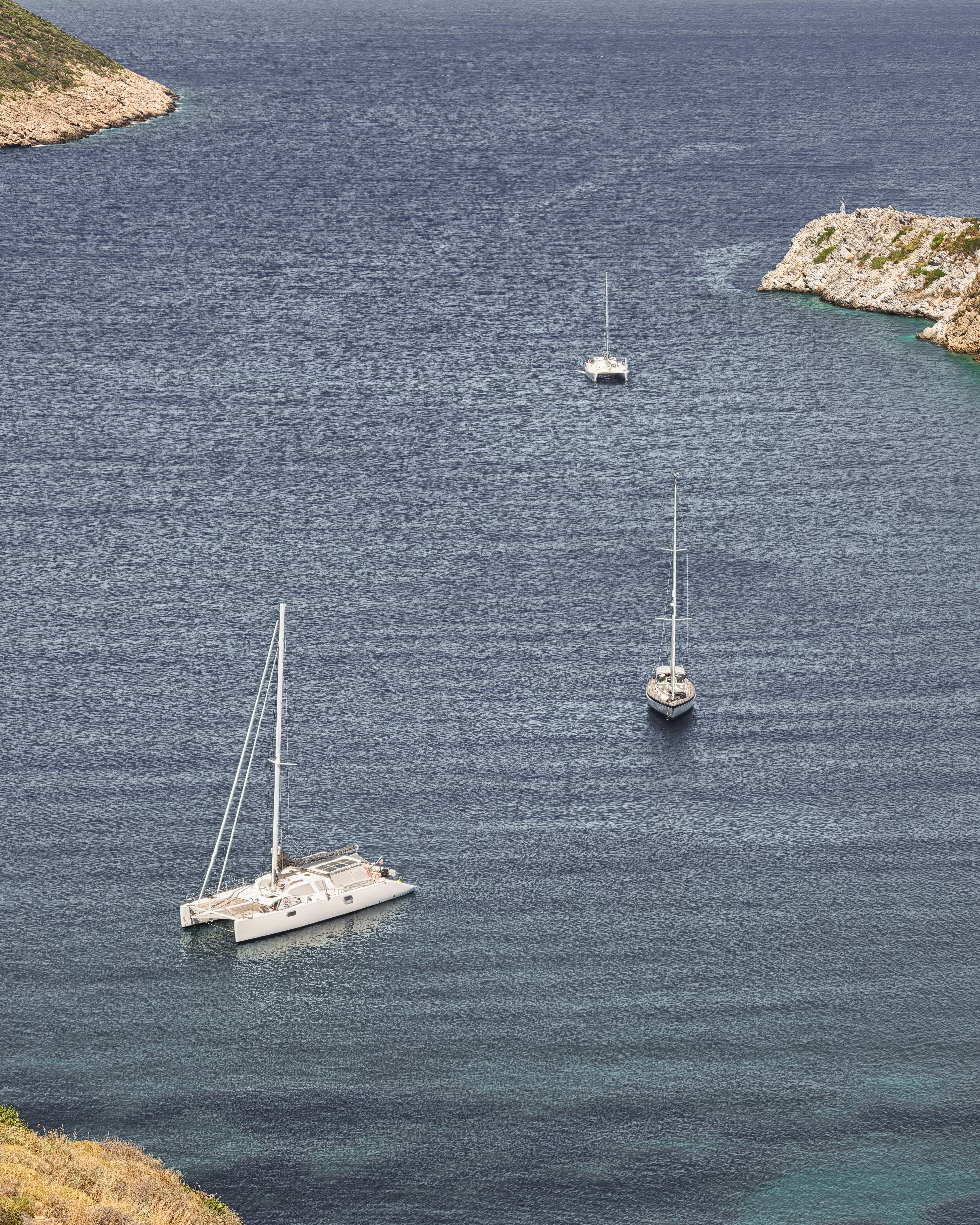 Two sailboats and a catamaran anchored in a calm blue bay