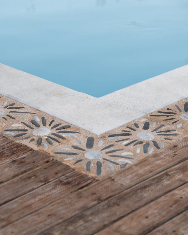 A swimming pool corner with a decorative pebble mosaic border and wooden