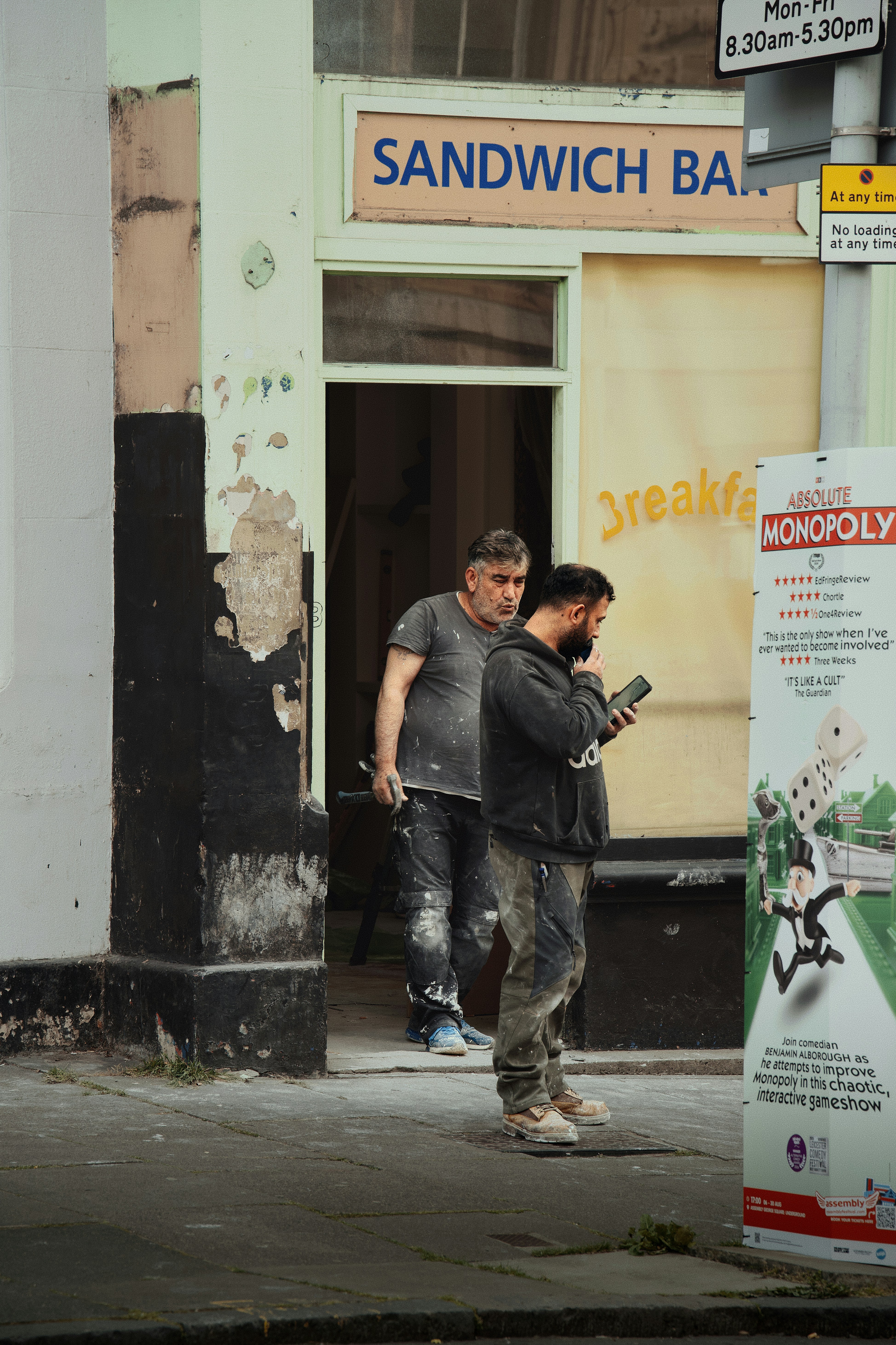 Two workers in paint-splattered clothes standing outside a shop doorway