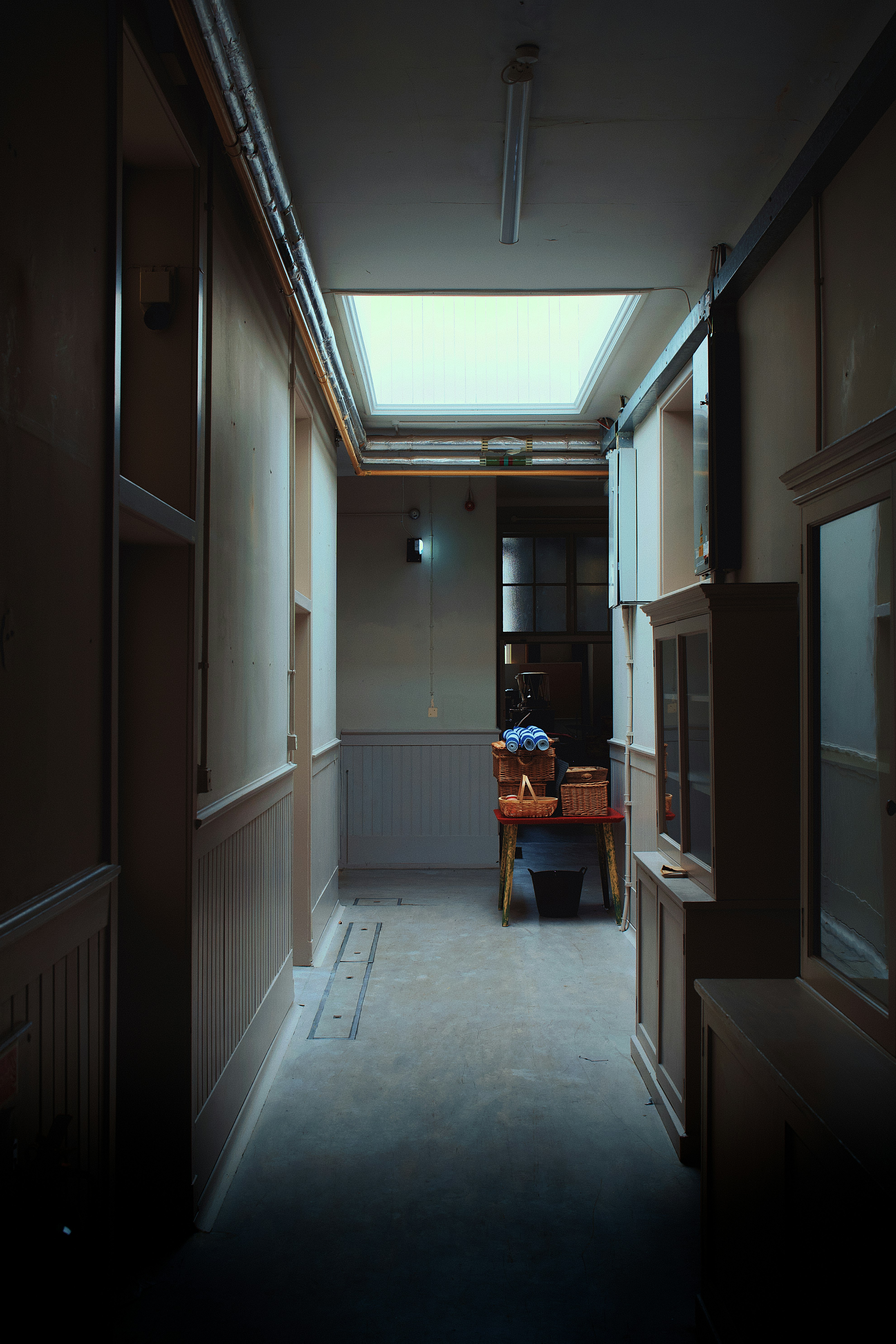 A narrow hallway with a skylight and wicker baskets on a red table
