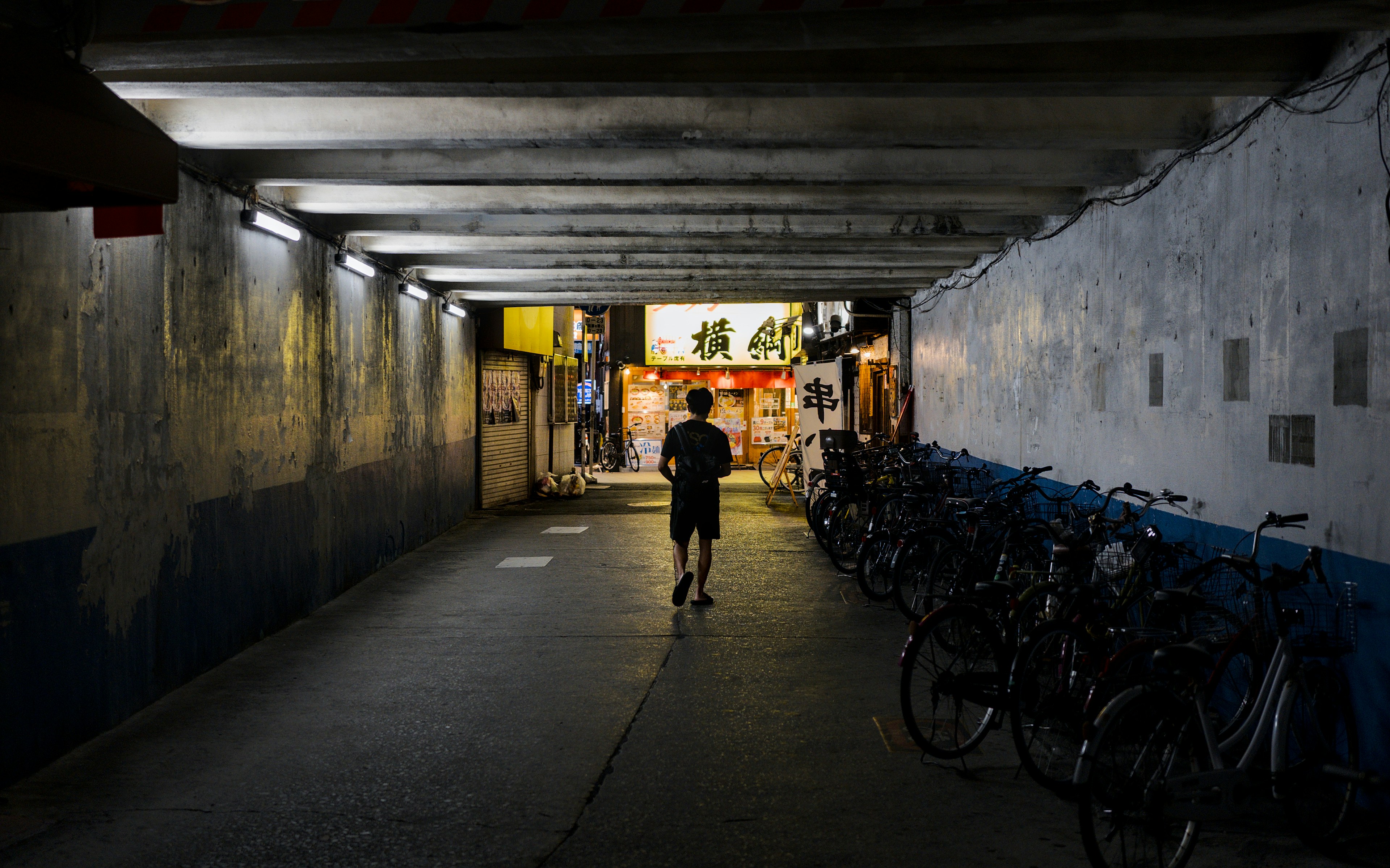 Une personne marchant dans un tunnel en béton avec des vélos garés vers une vitrine éclairée.