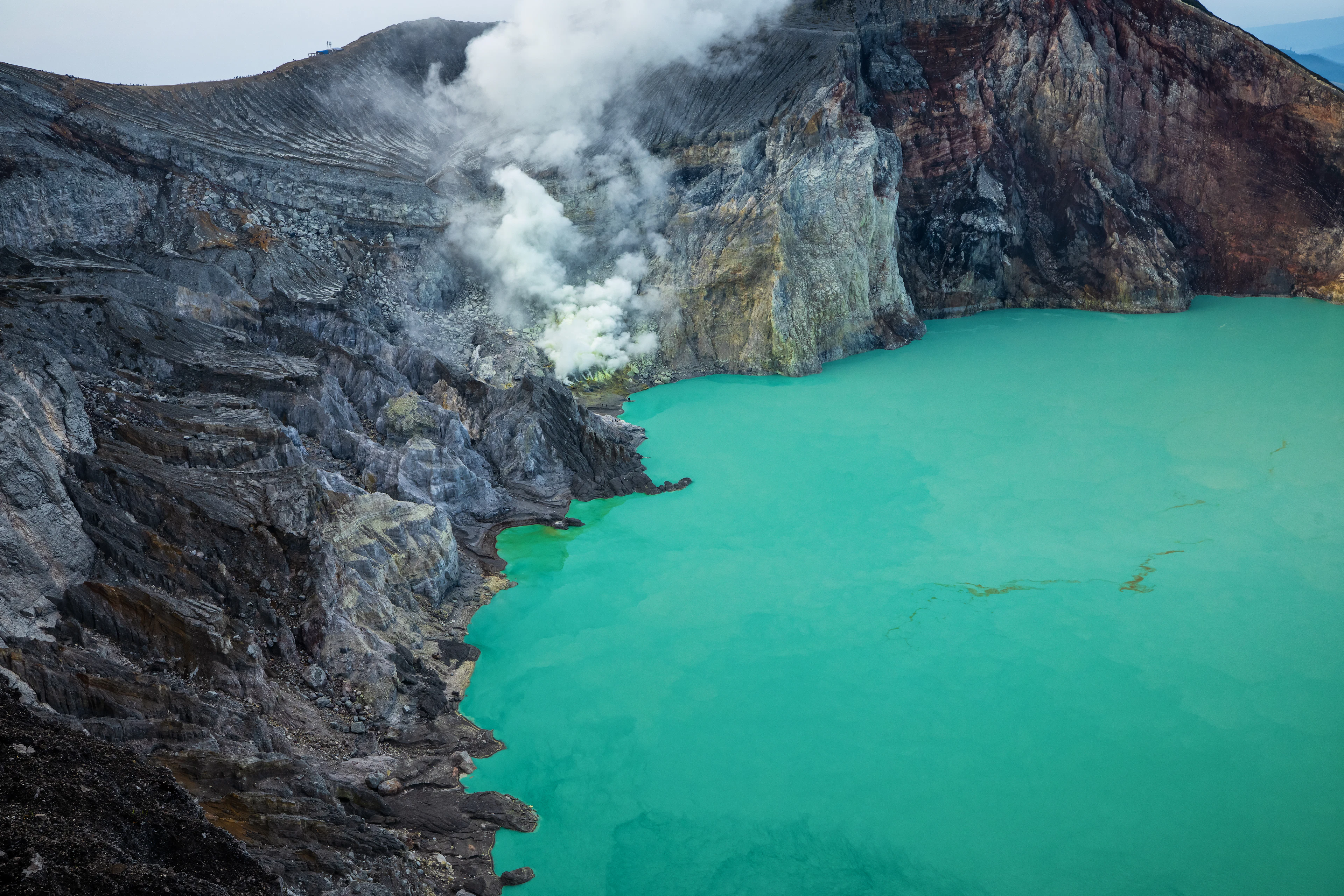 The turquoise acid lake of the Ijen crater, with sulphur steam above its rocky walls