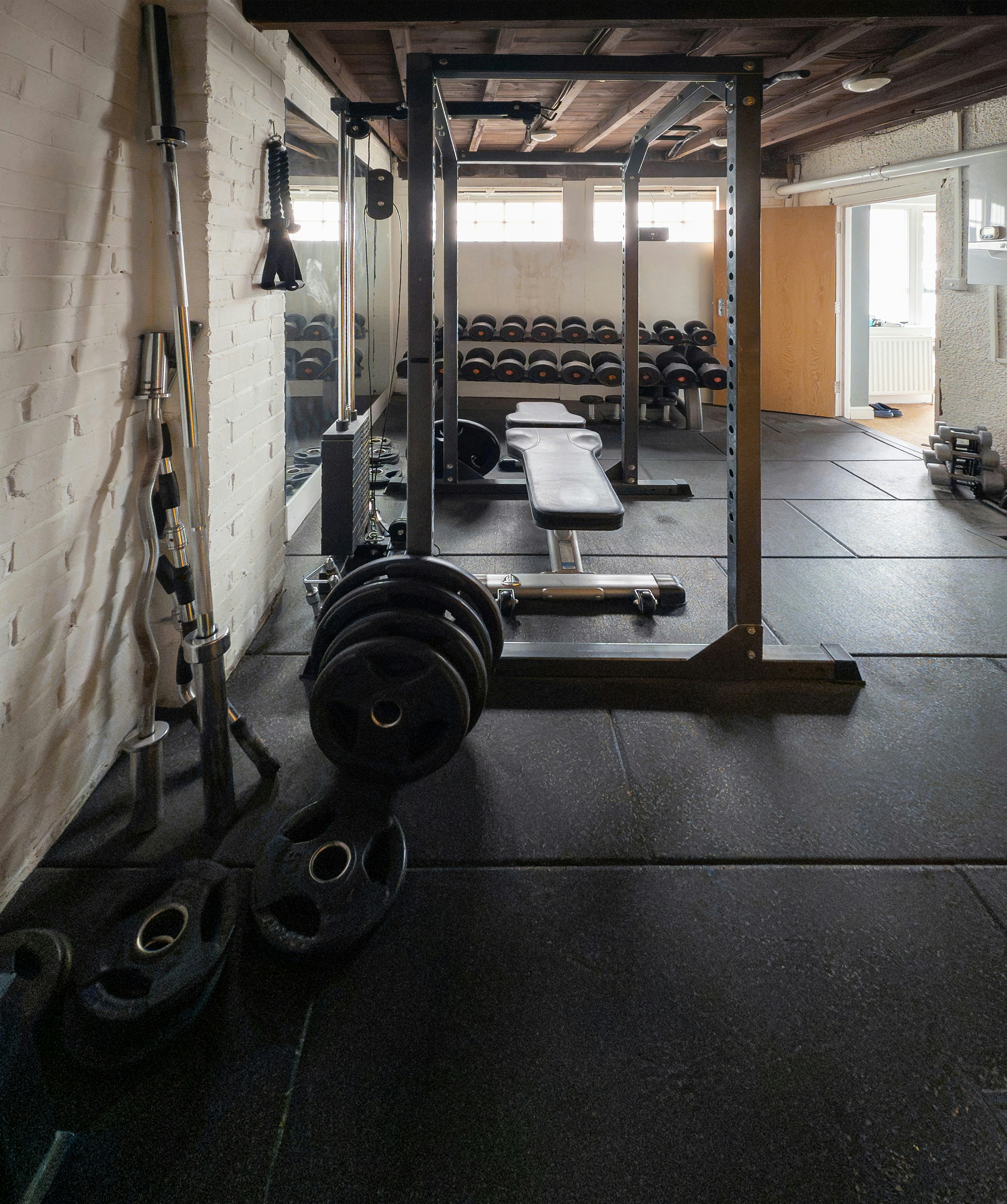 A home gym with a power rack, weight bench, and various plates on rubber flooring.