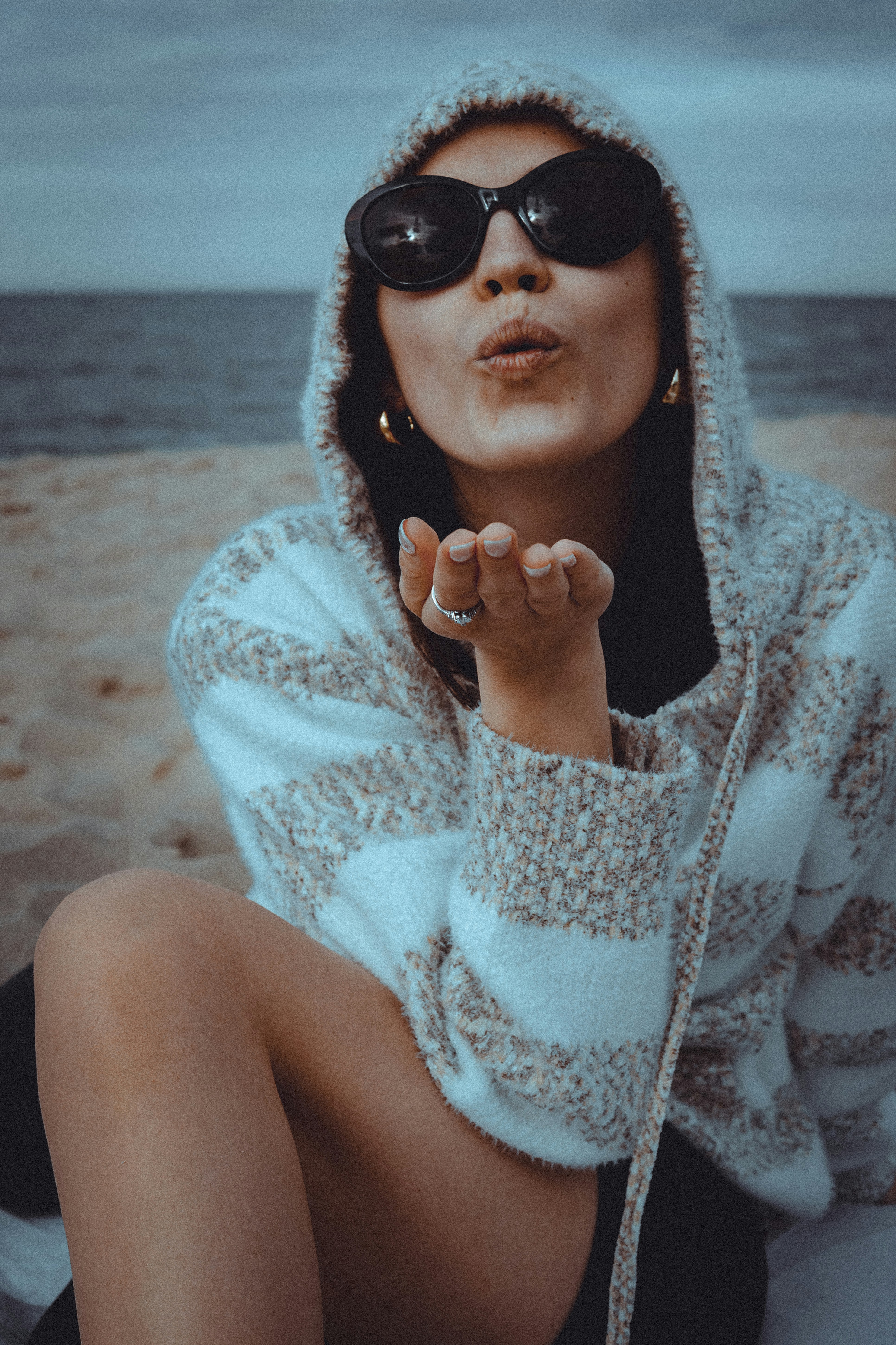 Una donna con un maglione con cappuccio che manda un bacio su una spiaggia sabbiosa