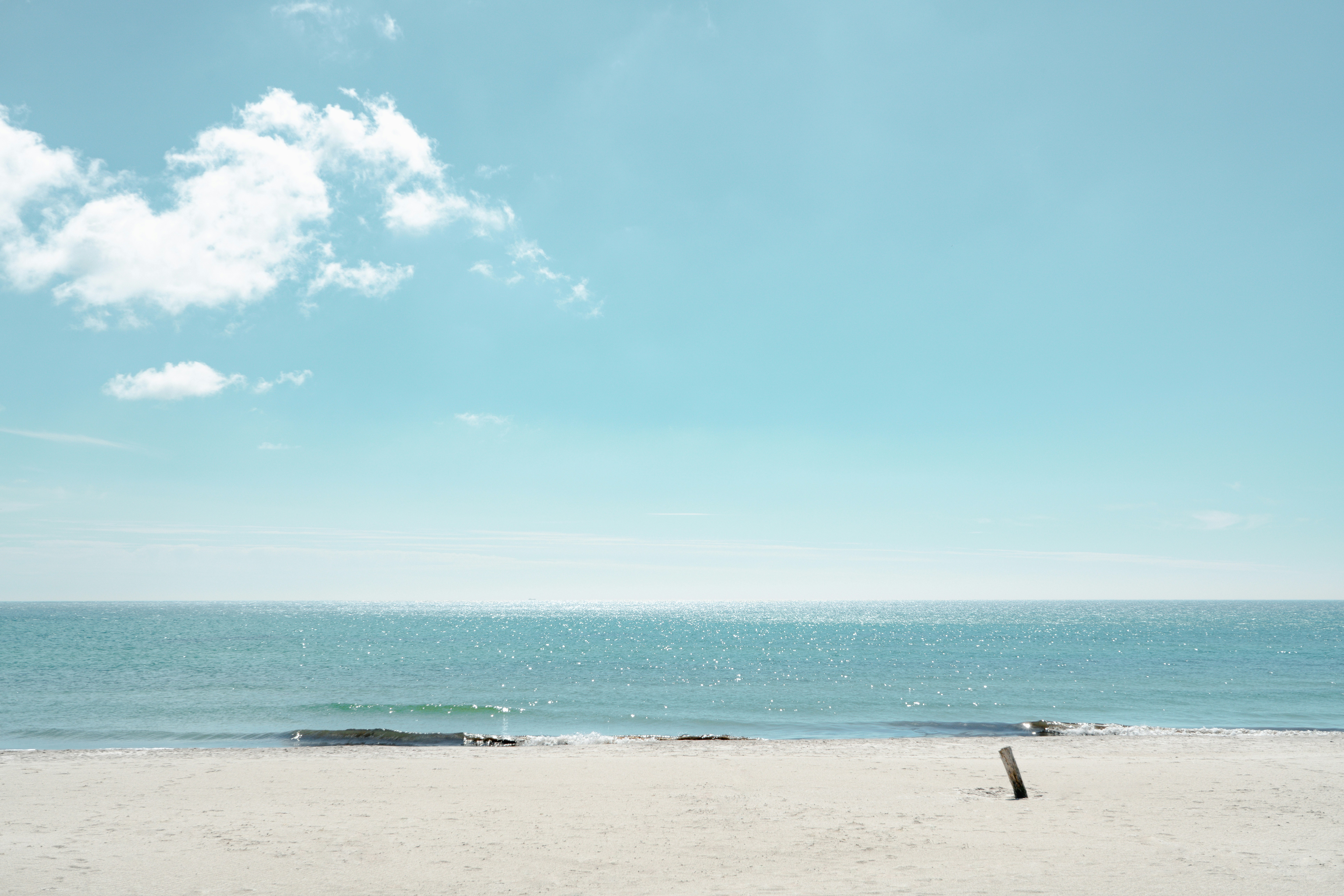A sandy beach with a single wooden post under a bright blue sky.