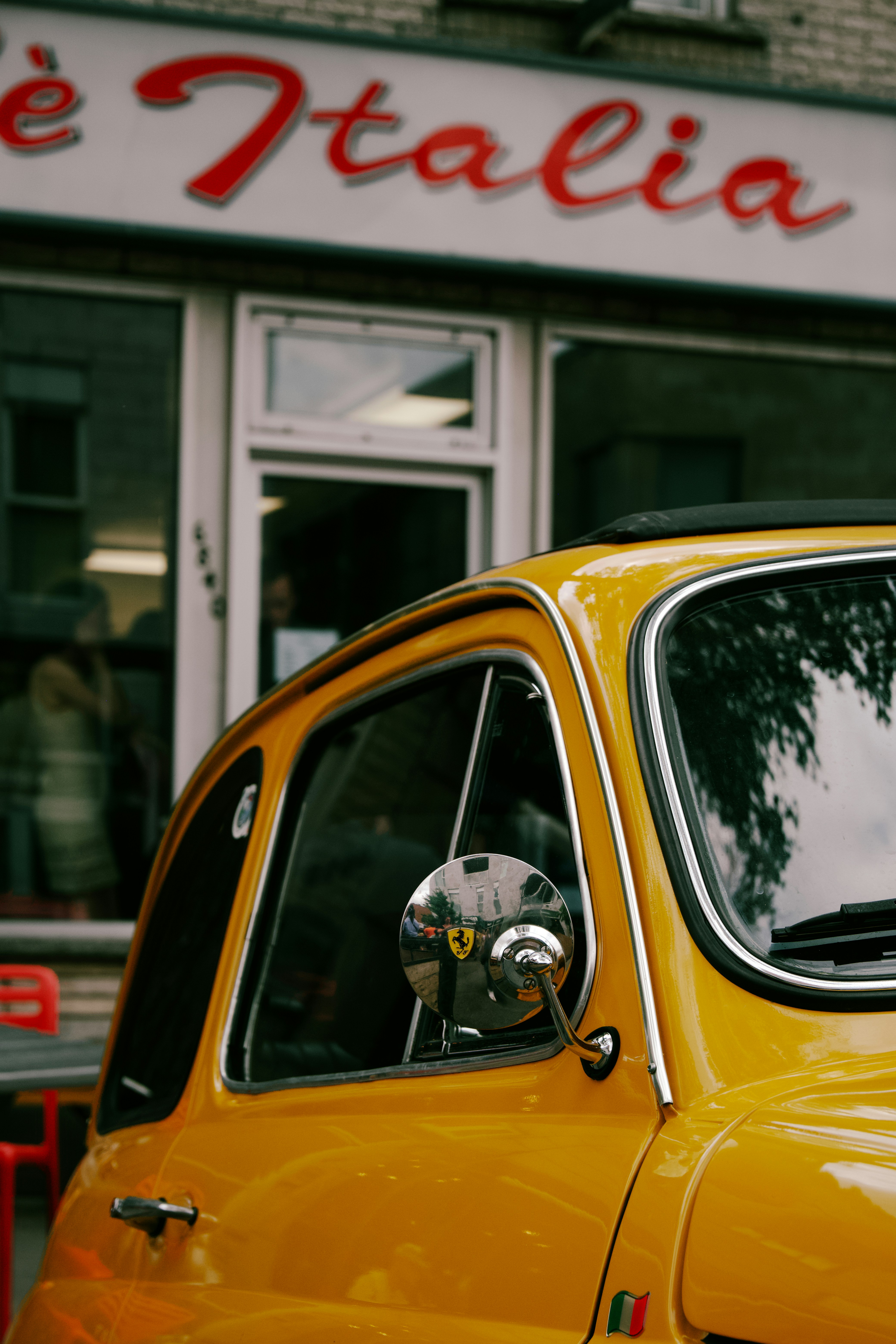 A yellow vintage car parked in front of a cafe named Italia.