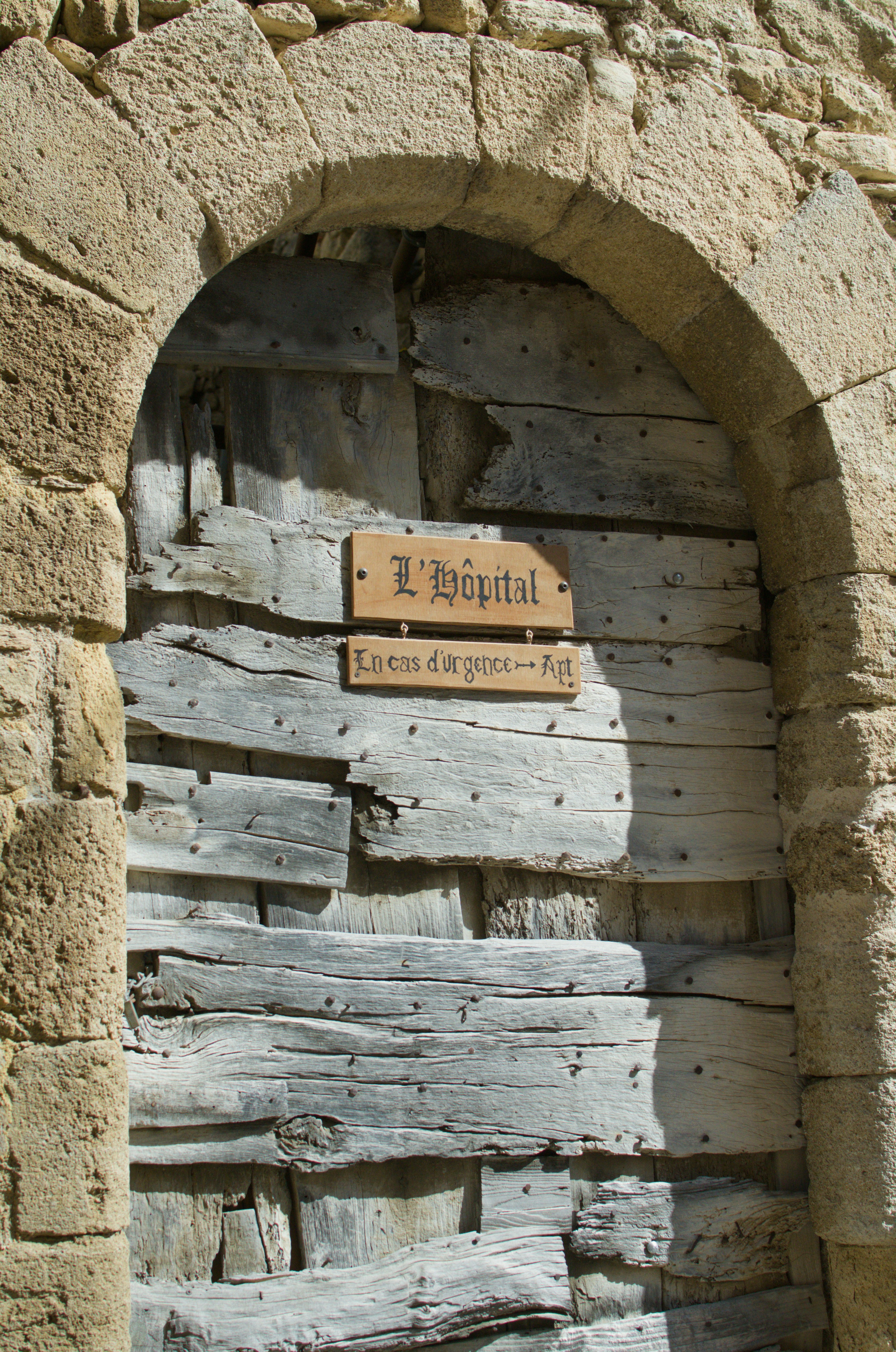 A wooden door in a stone arch with a sign reading "L'Hôpital"