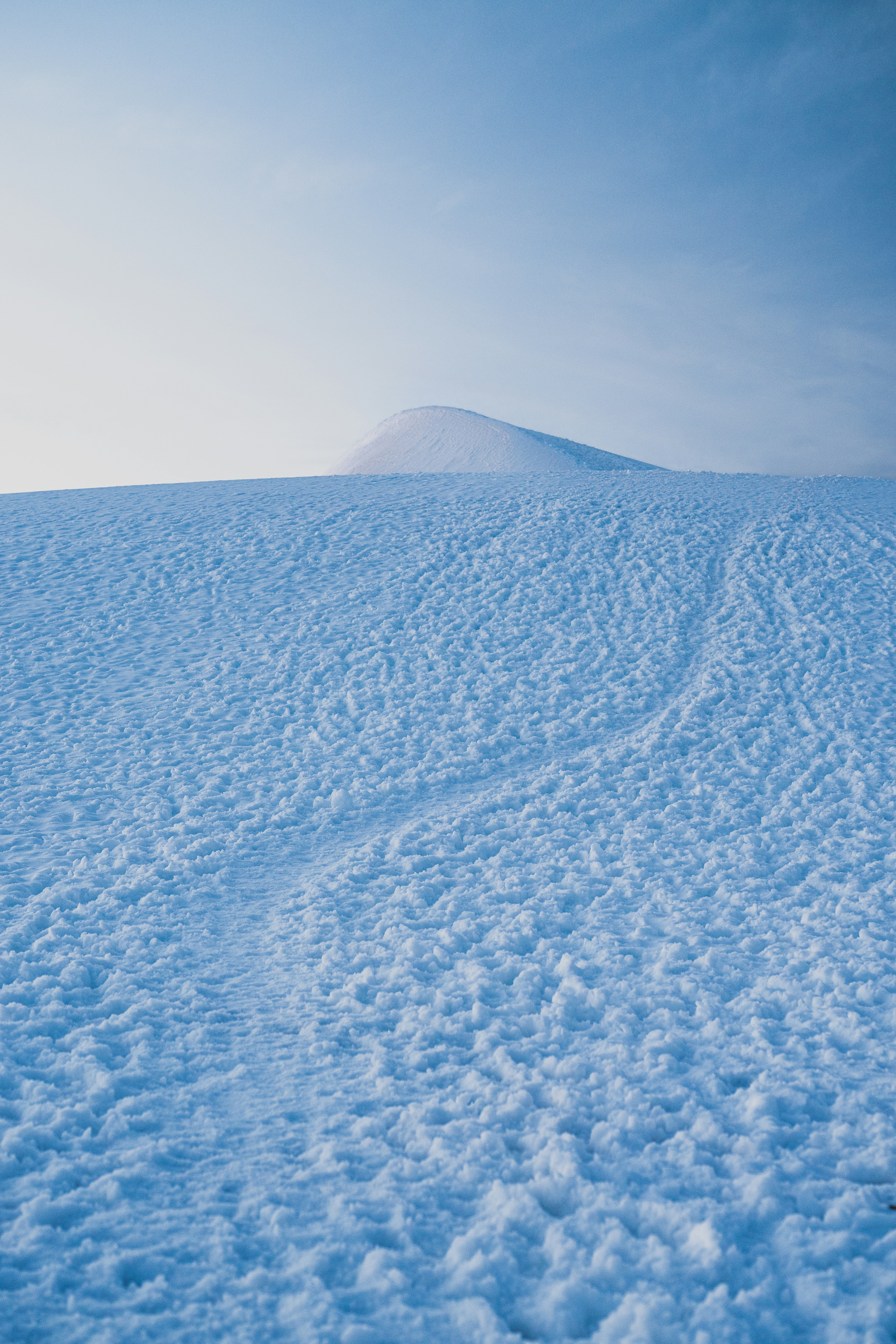 A snow-covered hill with faint footprints leading toward a rounded peak
