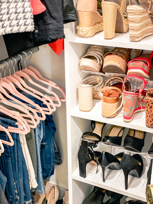Pink hangers with hanging clothes beside a white shelving unit filled with various shoes
