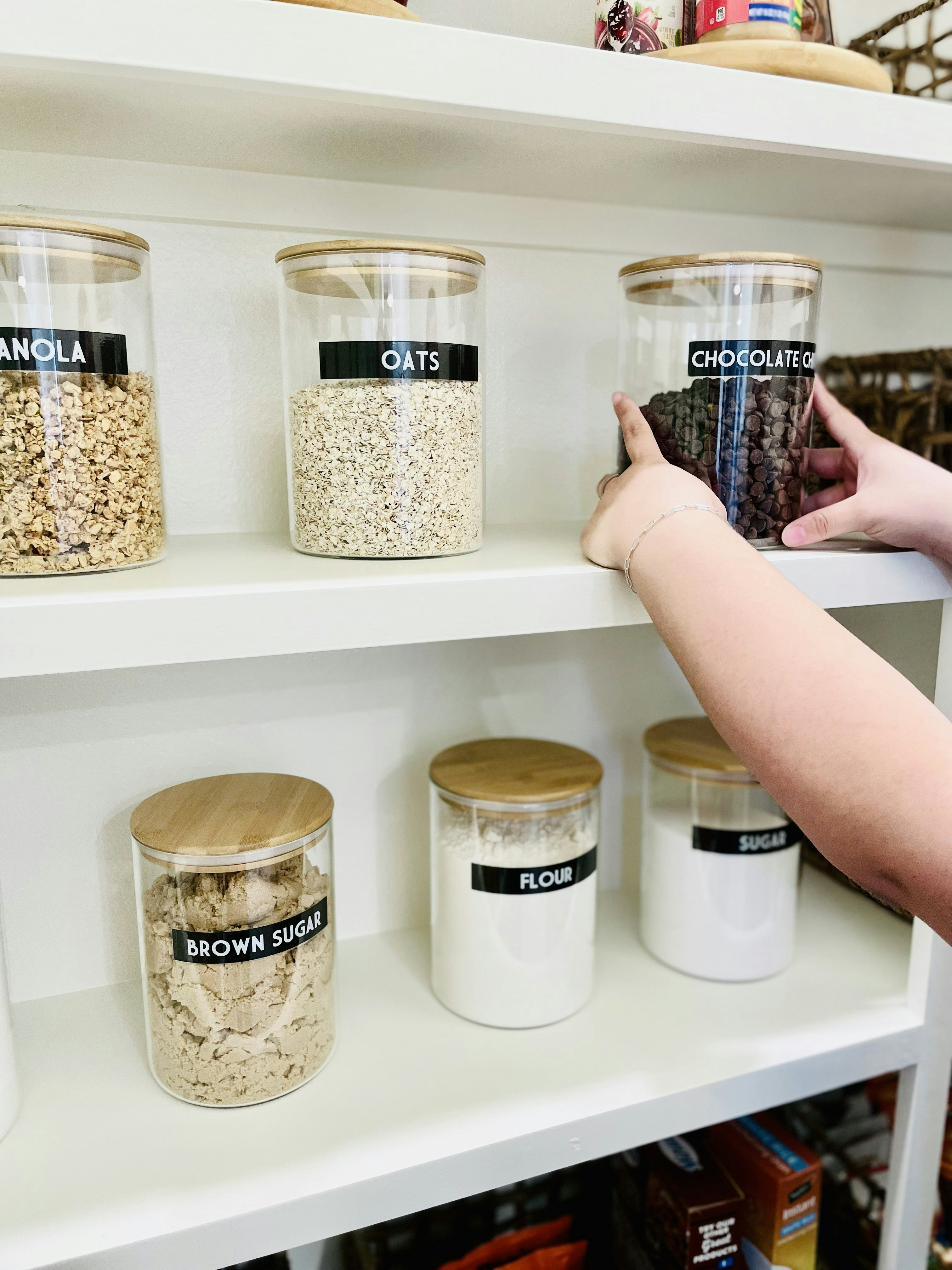 A person reaching for a glass jar of chocolate chips on a pantry shelf