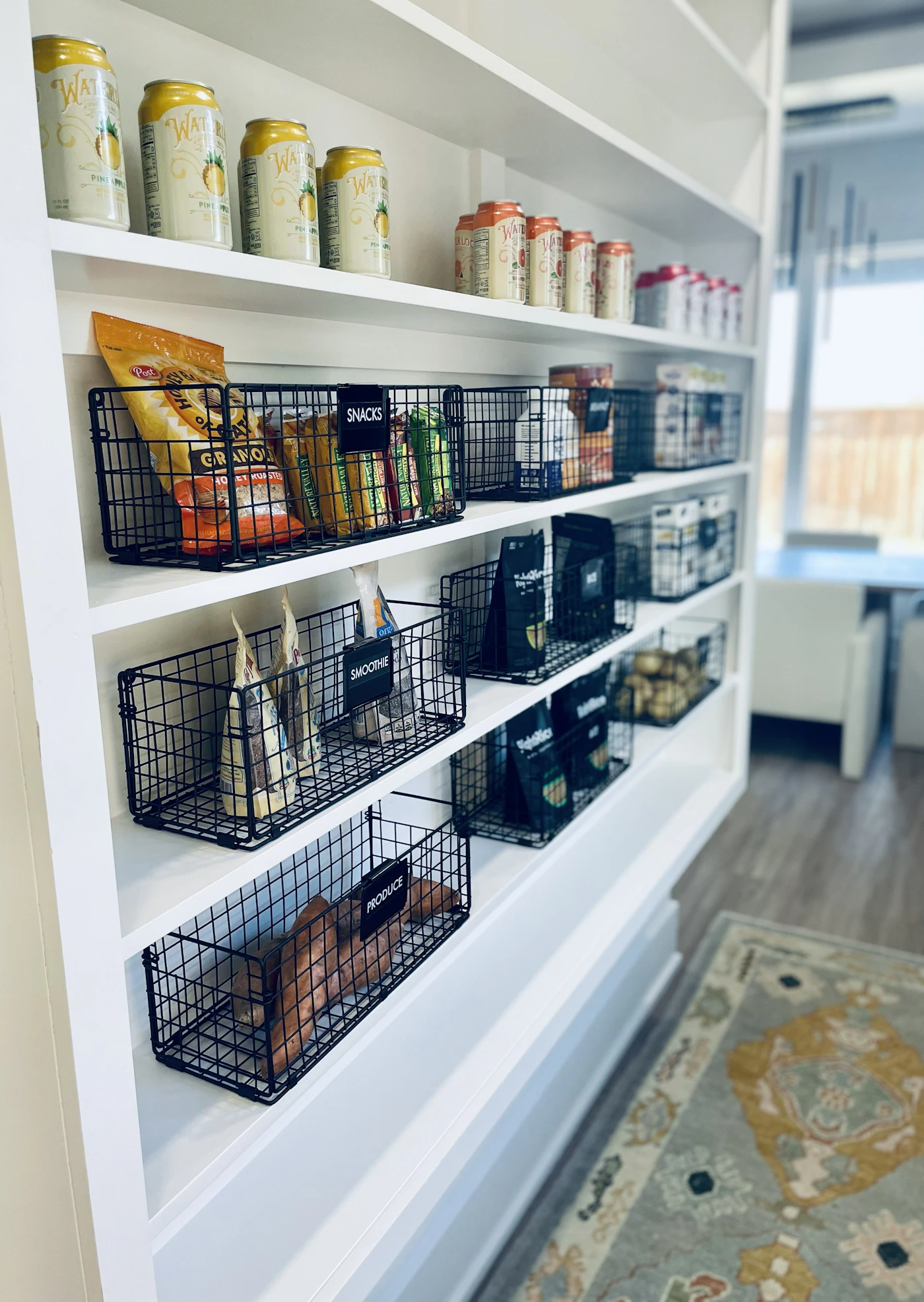 Organized pantry shelves with black wire baskets of snacks and produce