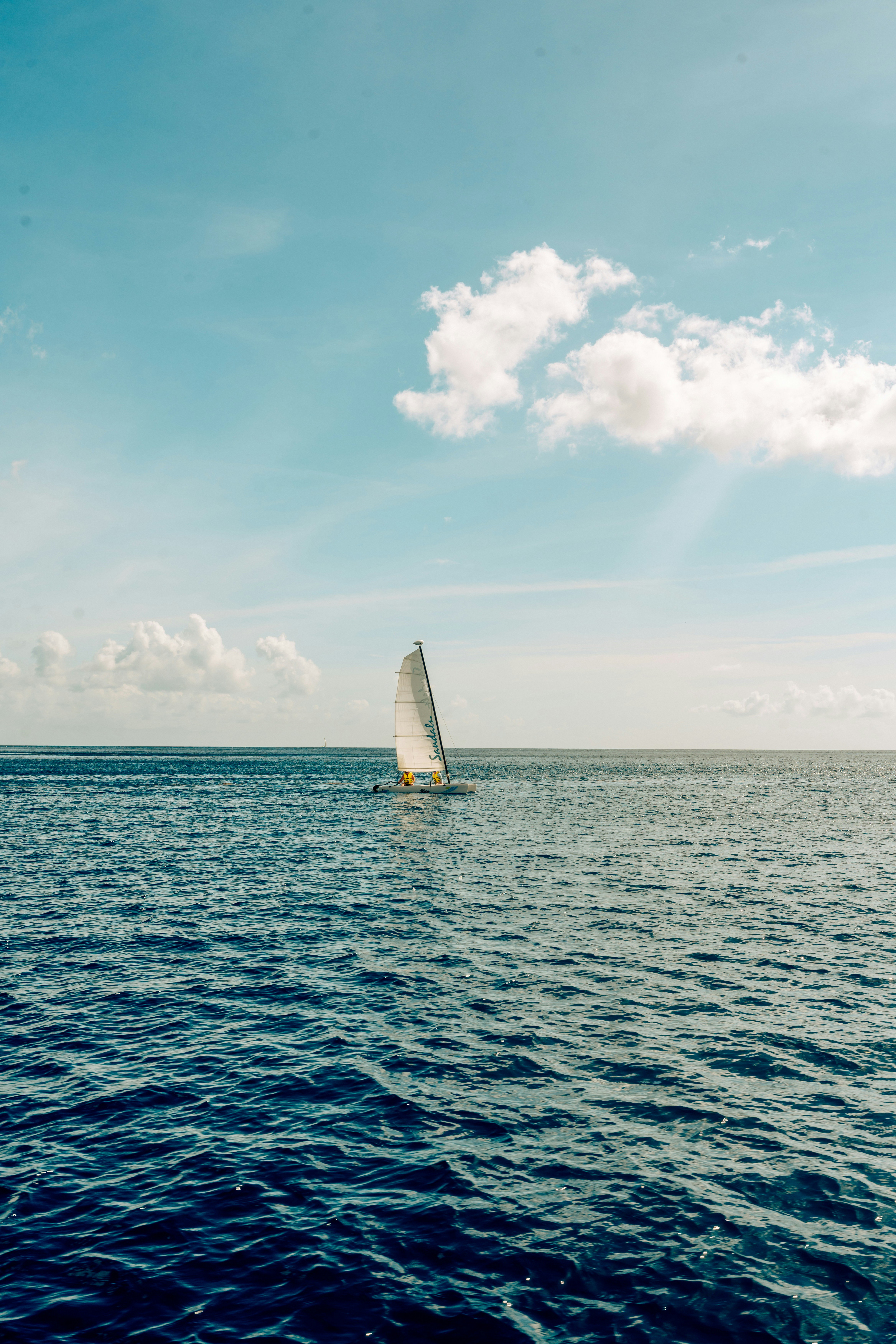 A small sailboat on the open blue ocean under a bright sky