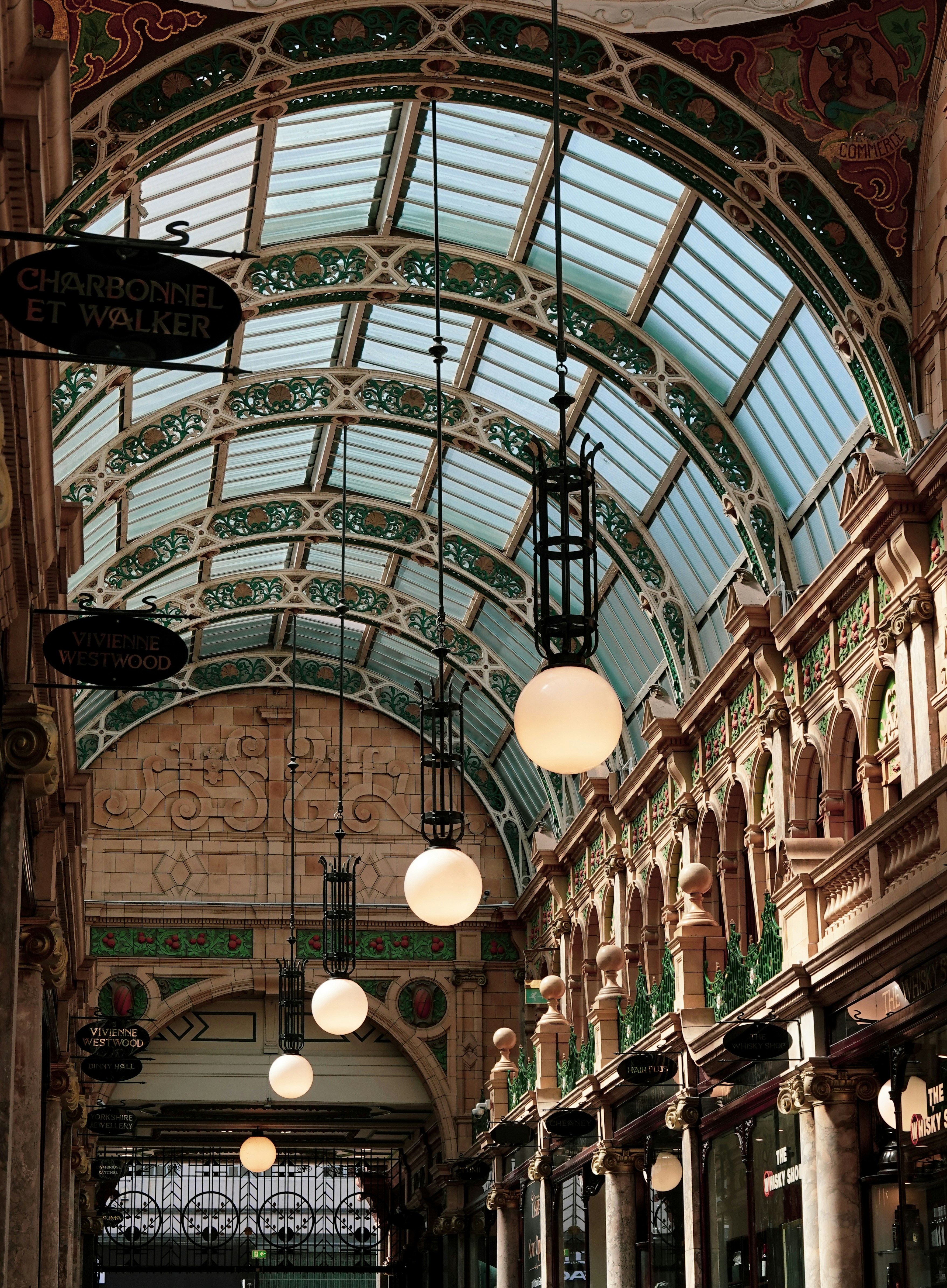 A glass-roofed Victorian shopping arcade with hanging globe lights and ornate architectural details
