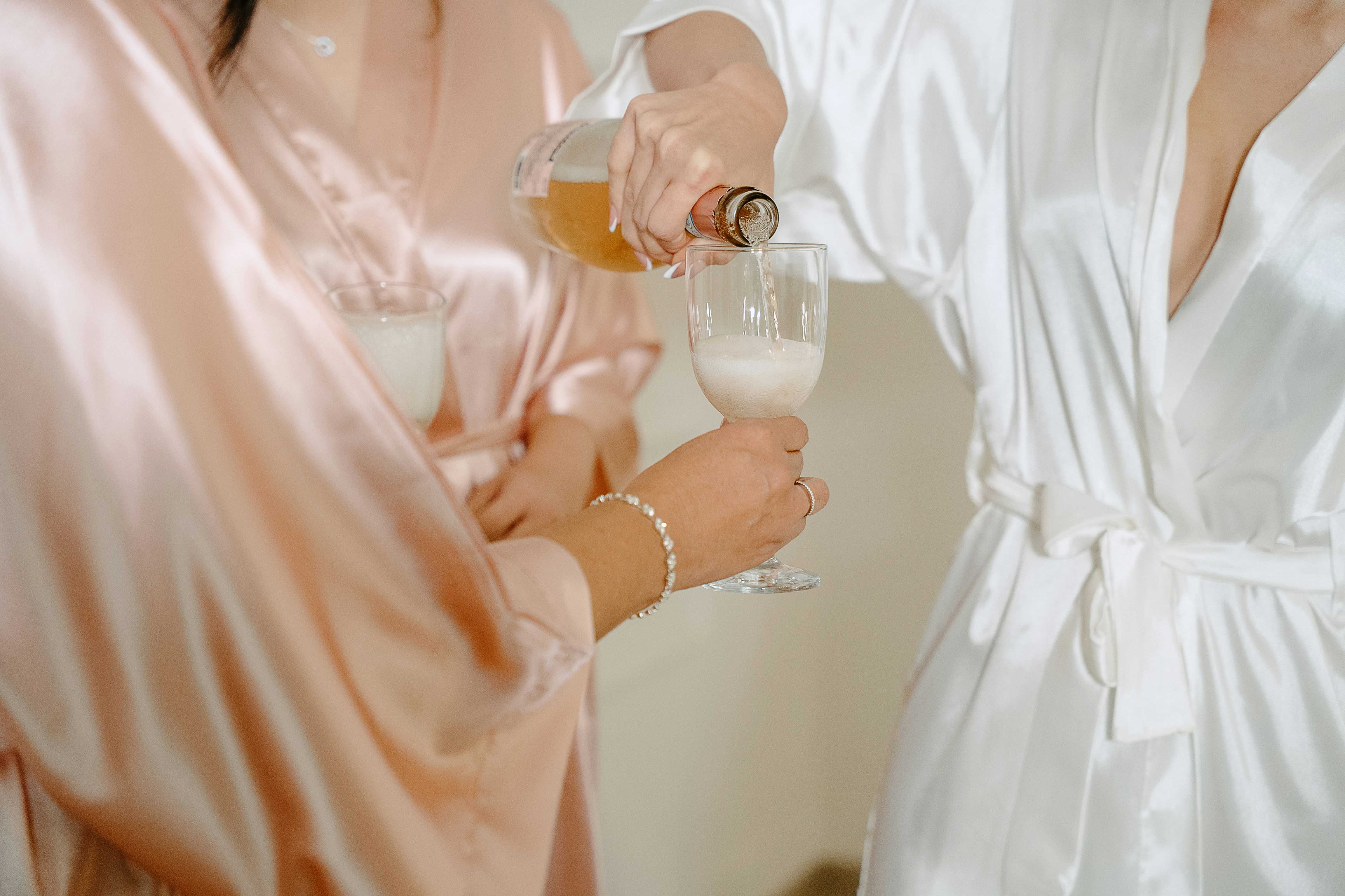A person in a white robe pouring champagne into a glass for another person.