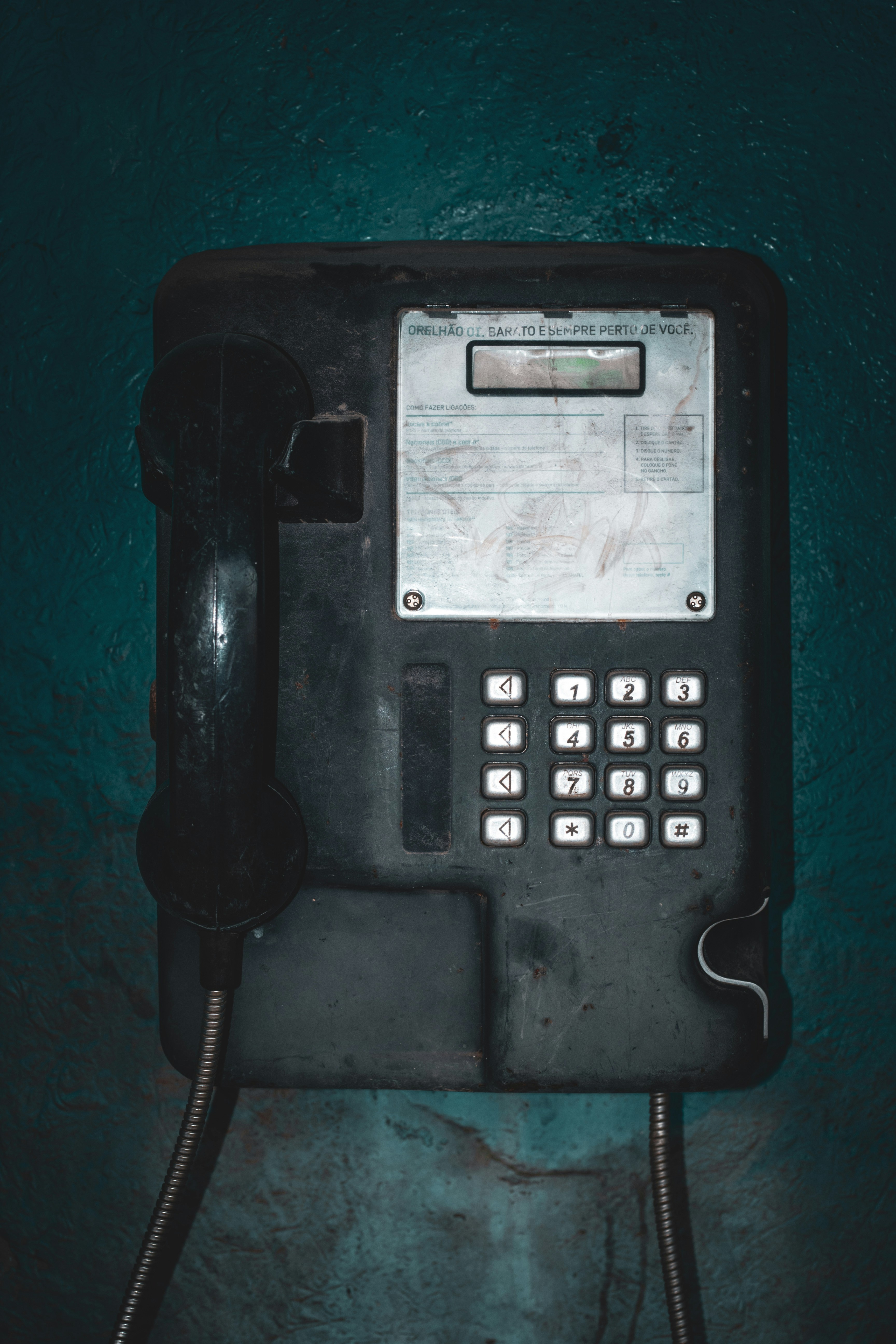 Telepon umum umum hitam yang sudah usang dipasang di dinding bertekstur teal gelap