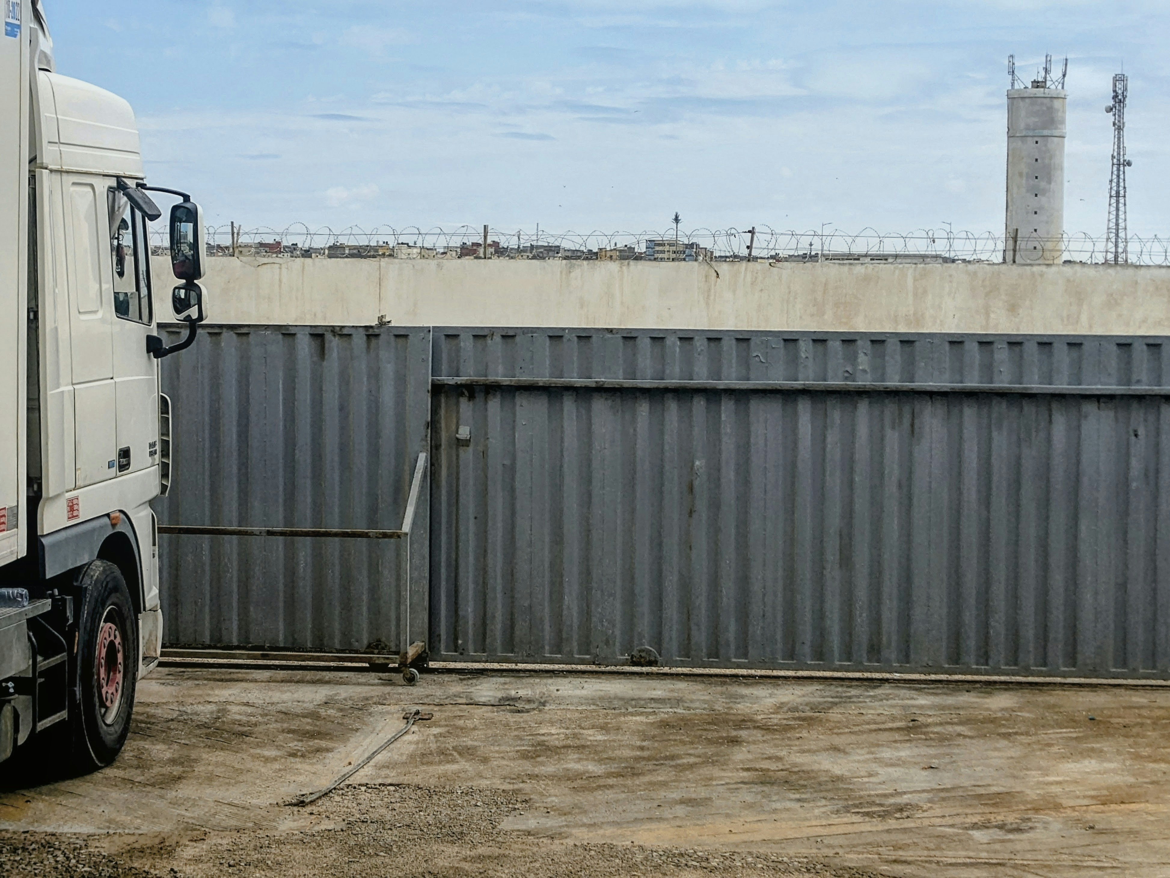 A white semi truck parked beside a large grey metal sliding gate at an industrial site