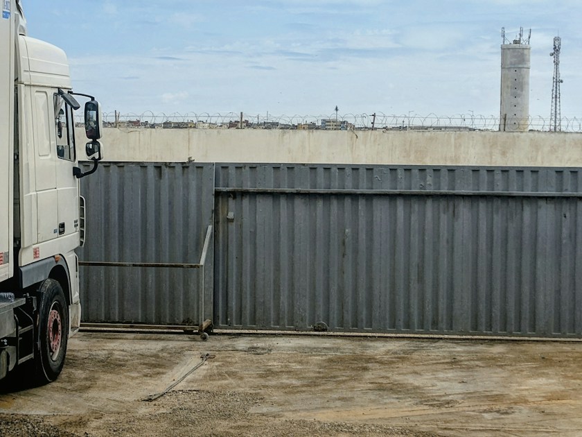 A white semi truck parked beside a large grey metal sliding gate