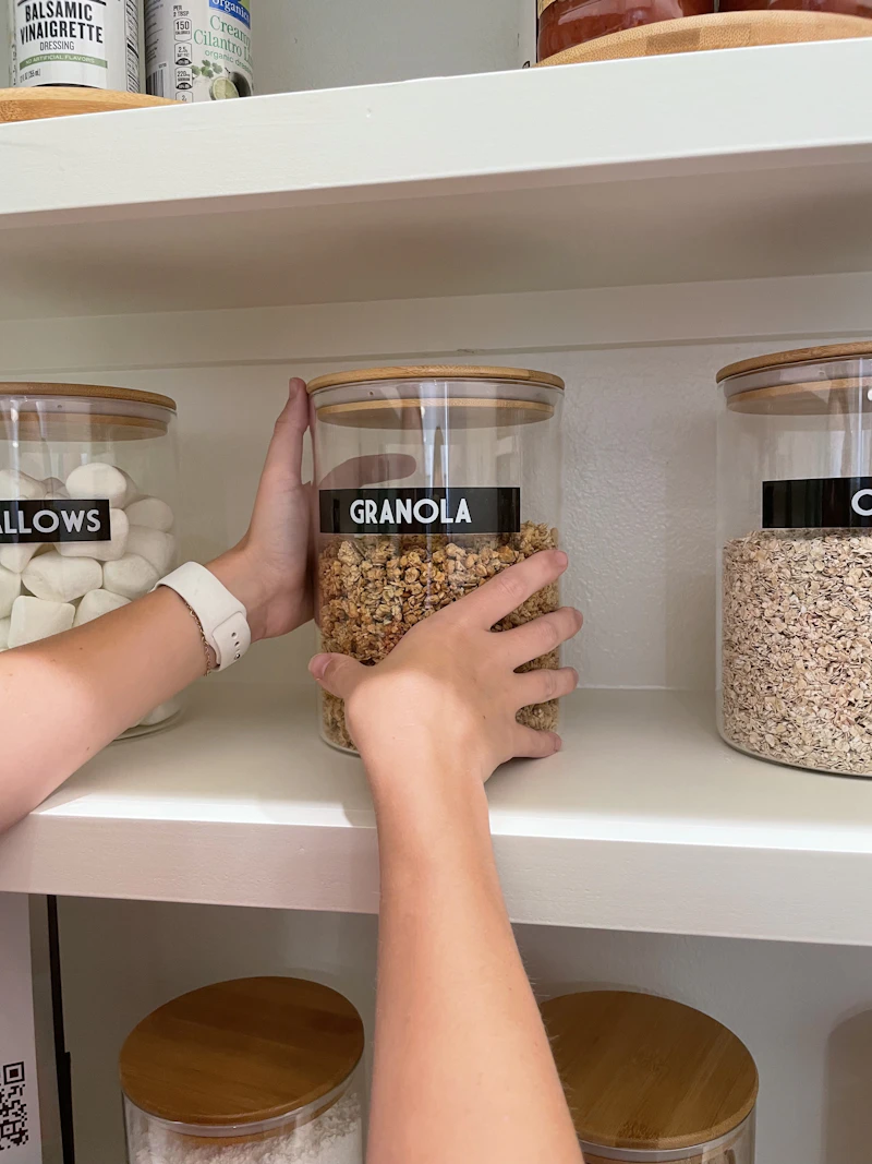 Hands organizing labeled jars on a pantry shelf