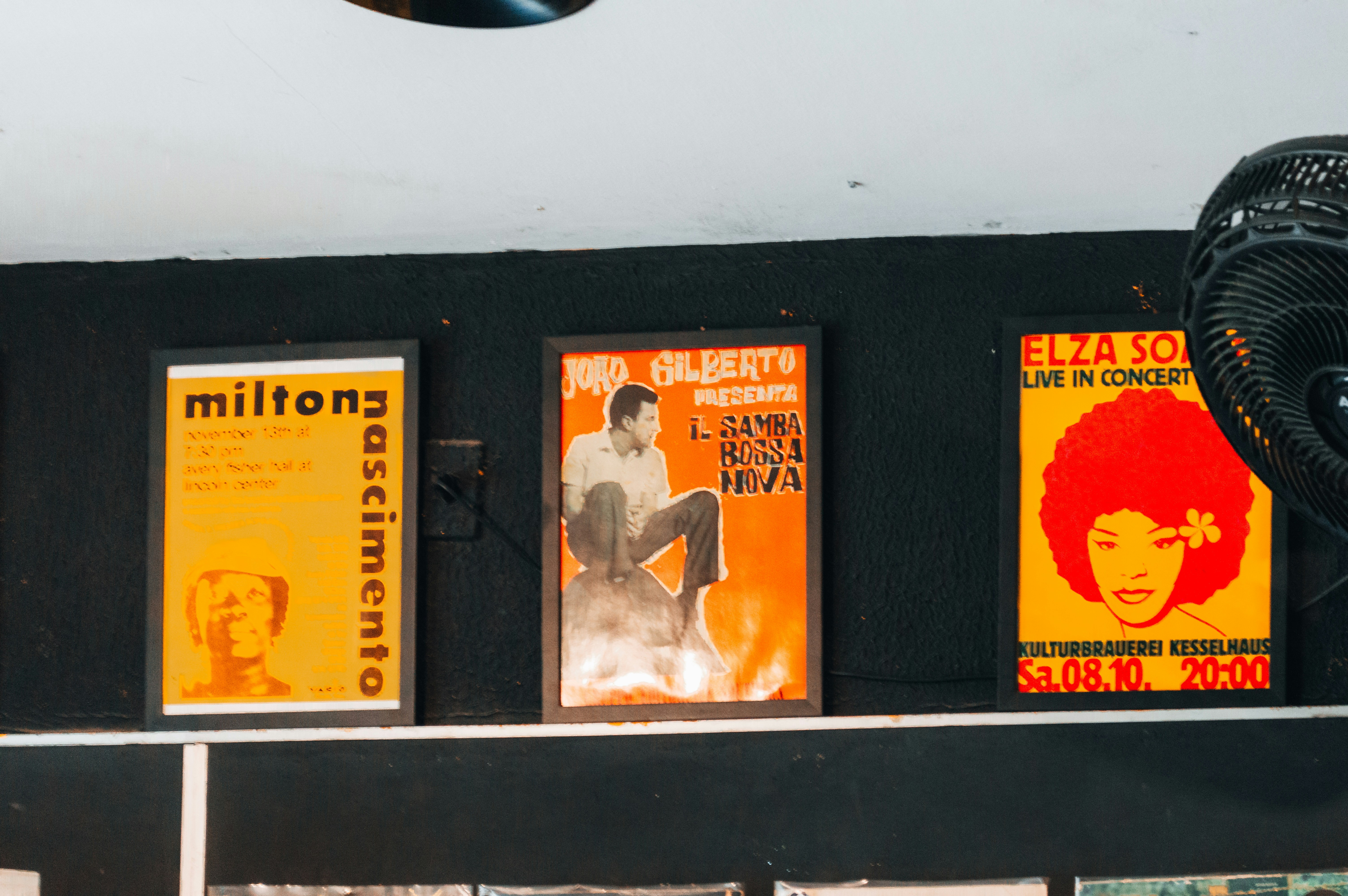 Three framed music posters hanging on a black wall above a white ledge